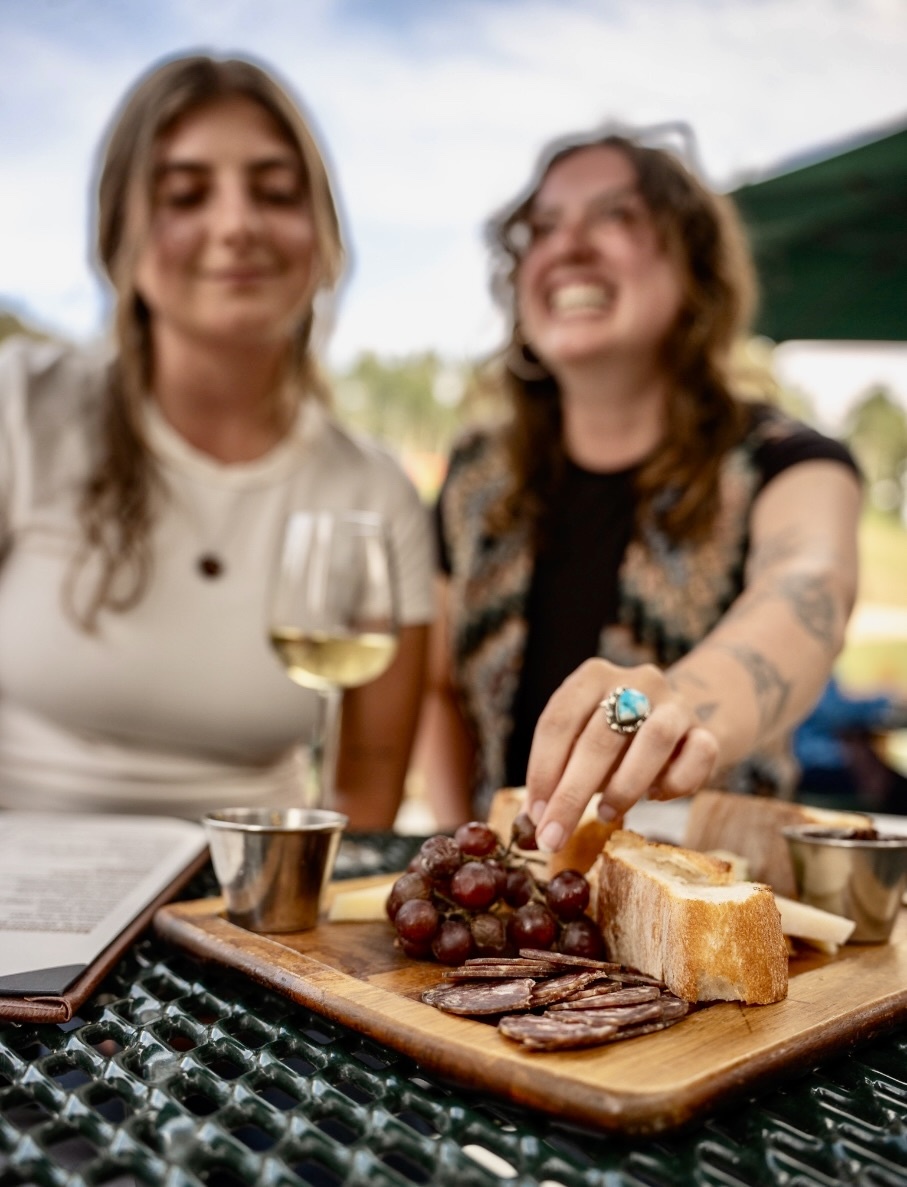 Two people enjoying wine and a charcuterie board outdoors.