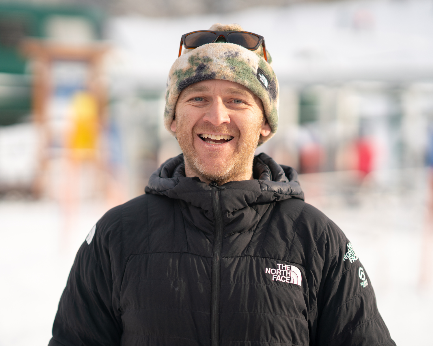 Man smiling in winter clothing, snowy background.