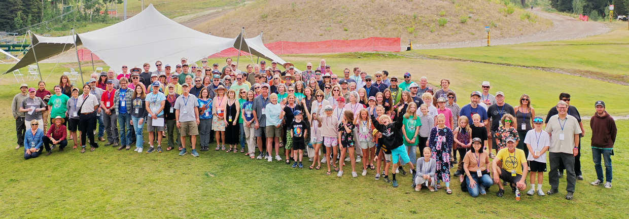 Large group of people gathered on grass with a tent in the background.