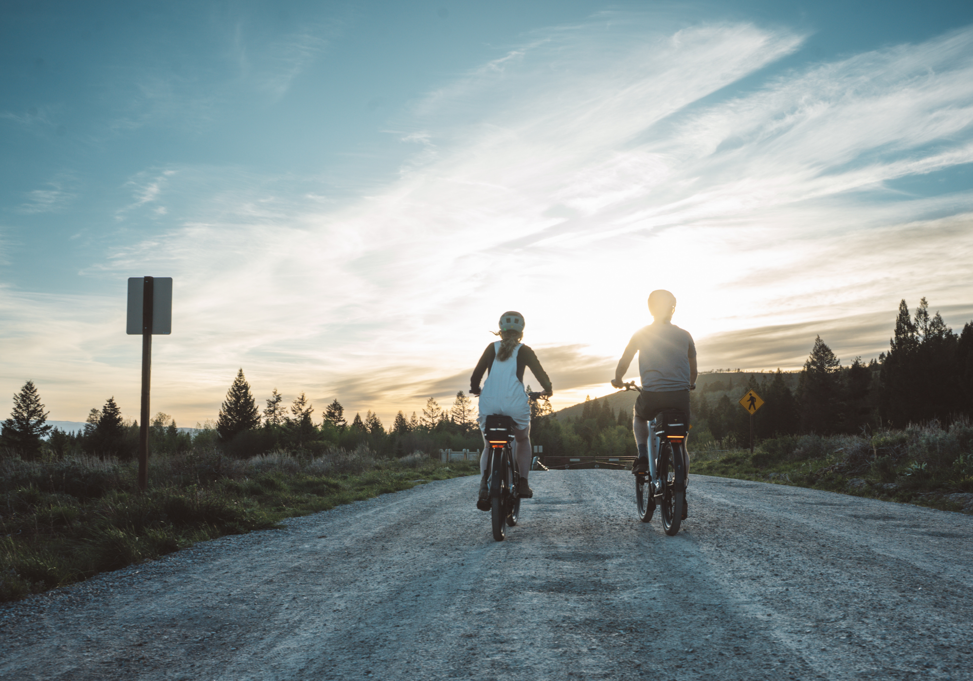 Two people cycling on a rural road at sunset.