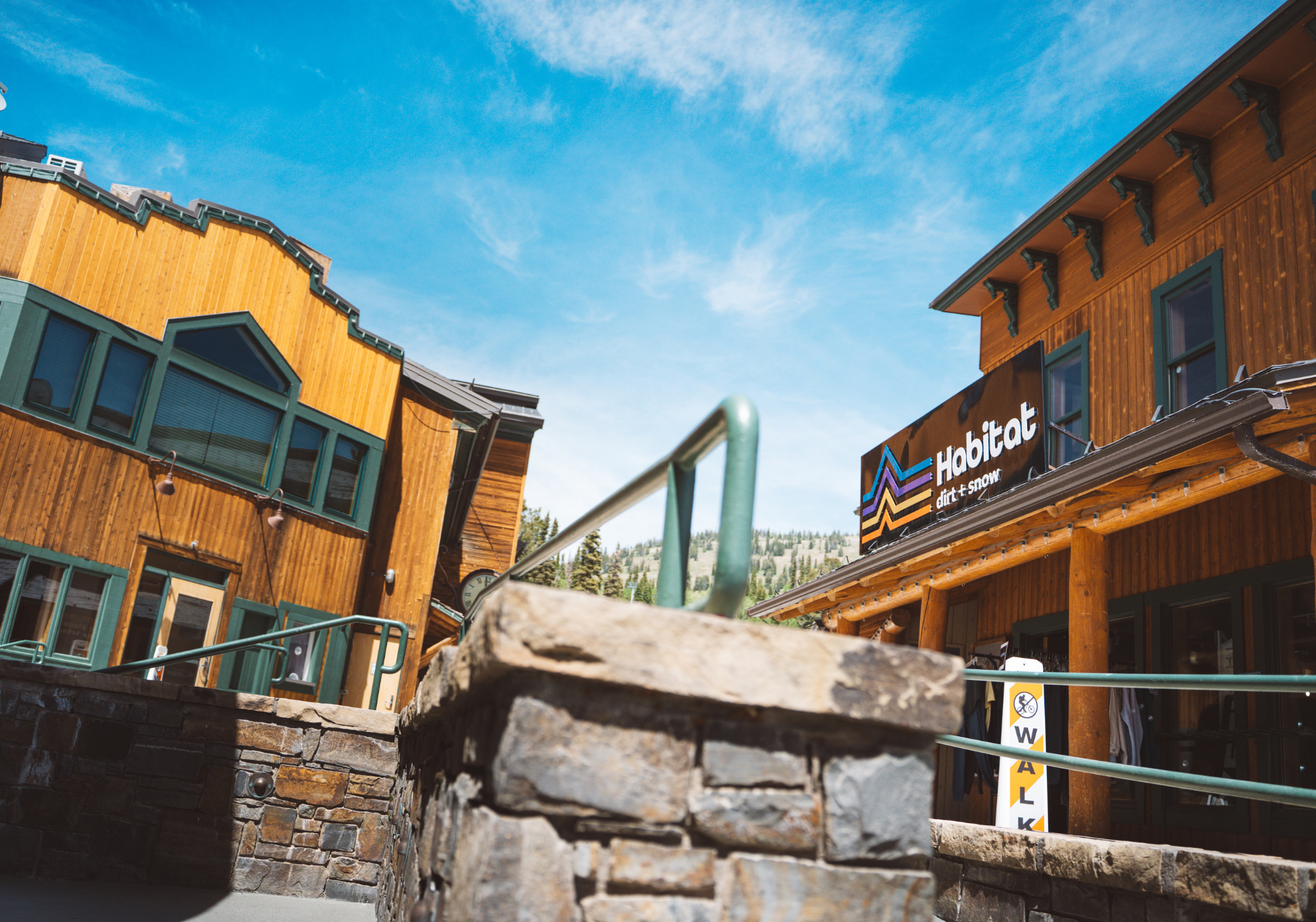 Wooden buildings under a blue sky, with a stone railing in front.