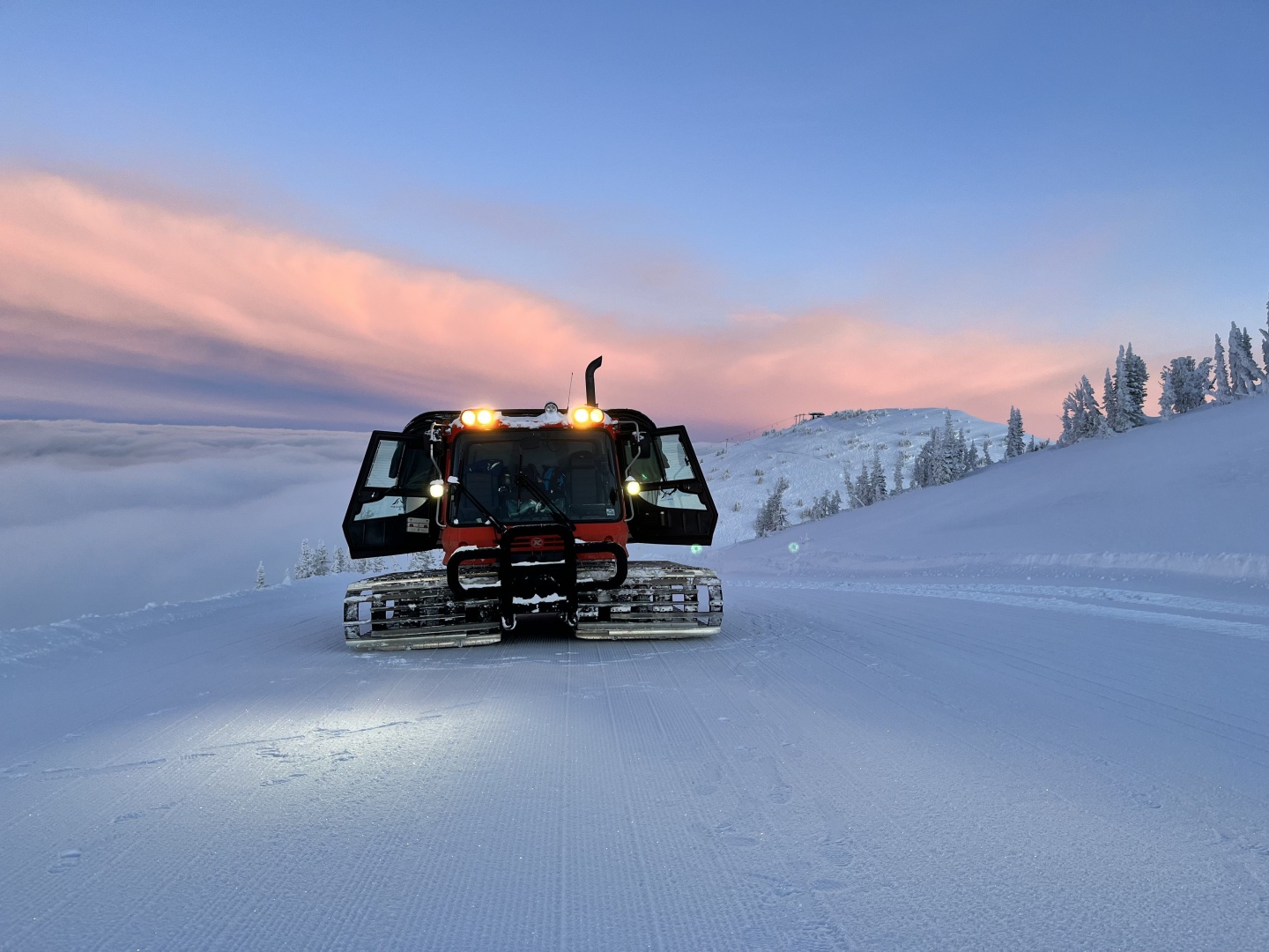 A snowcat grooming a mountain at sunrise