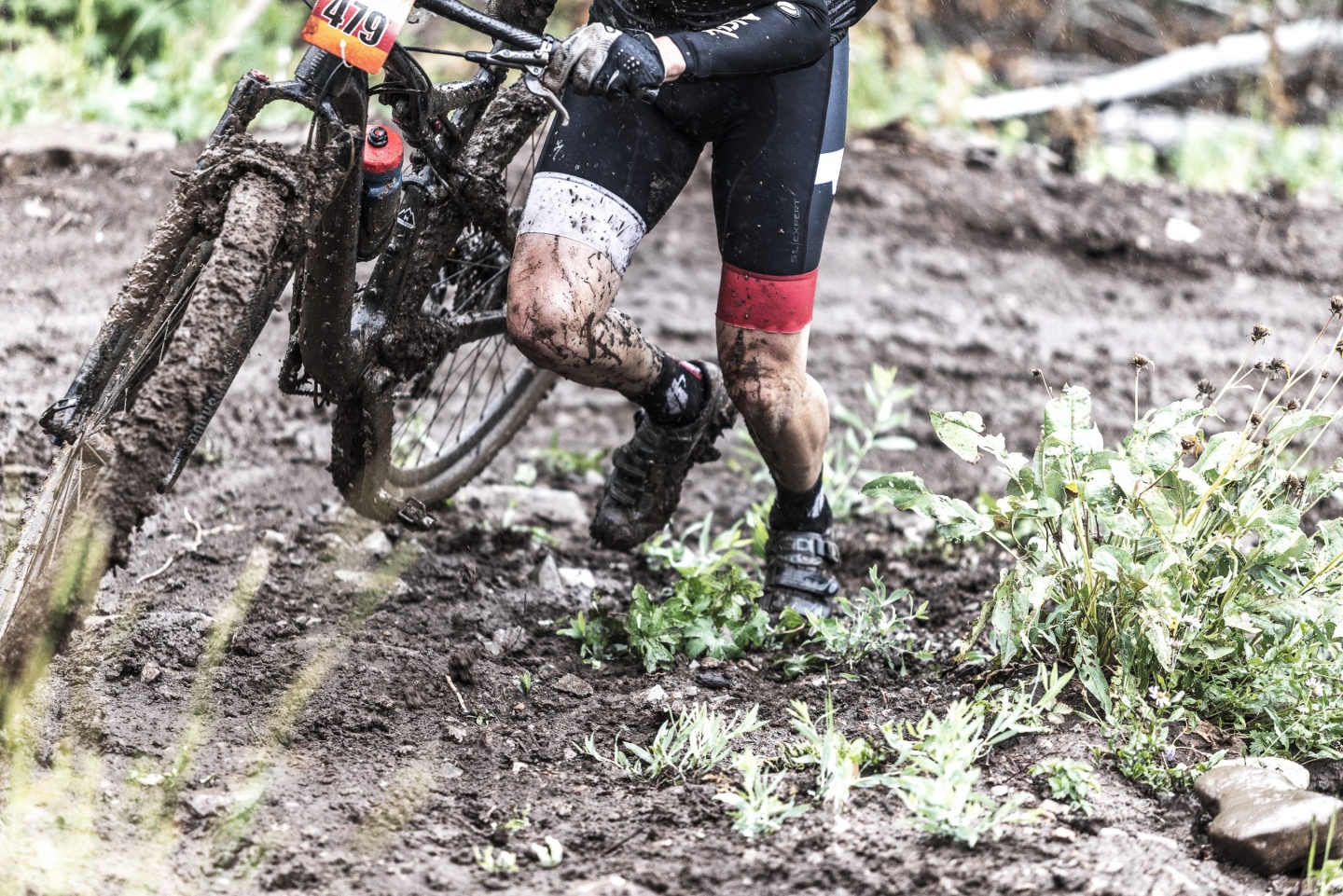 A cyclist walking their bike up a muddy trail
