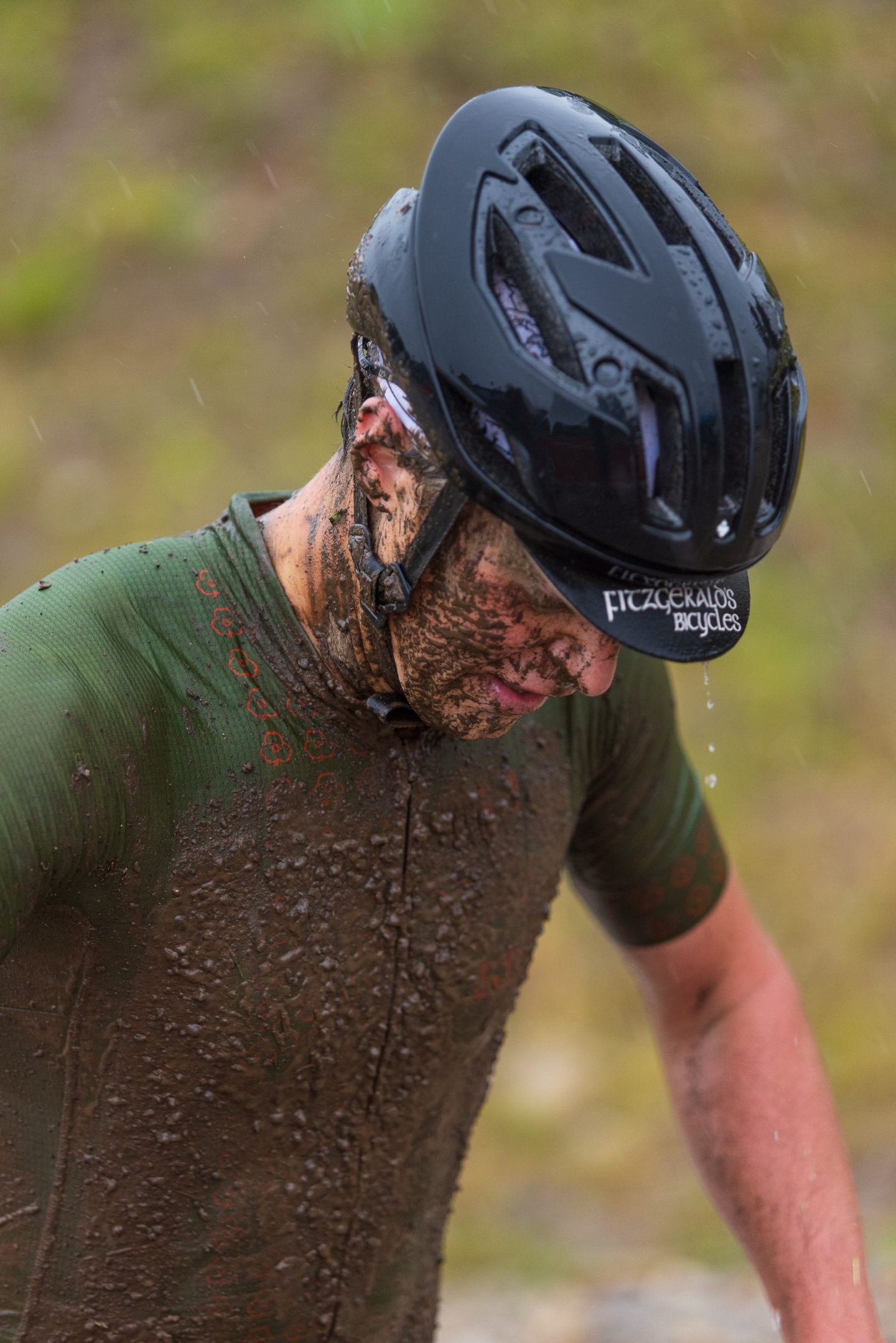 A cyclist standing in the rain covered in mud