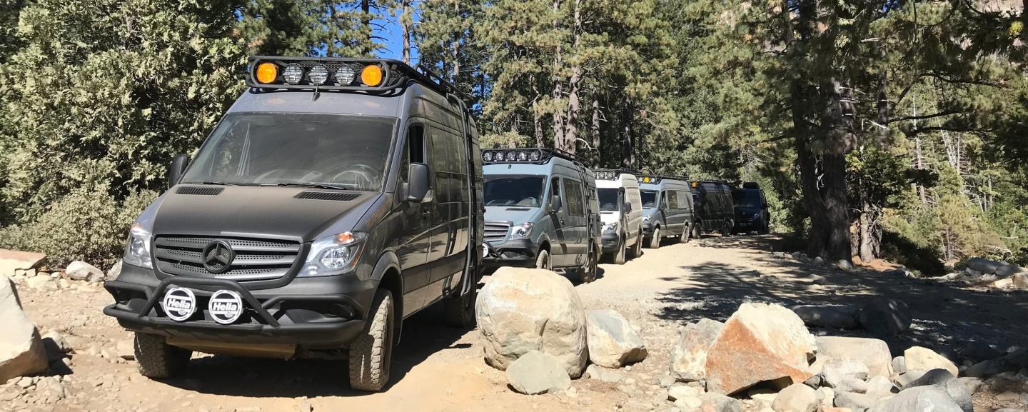Six camper vans parked outside in a campground