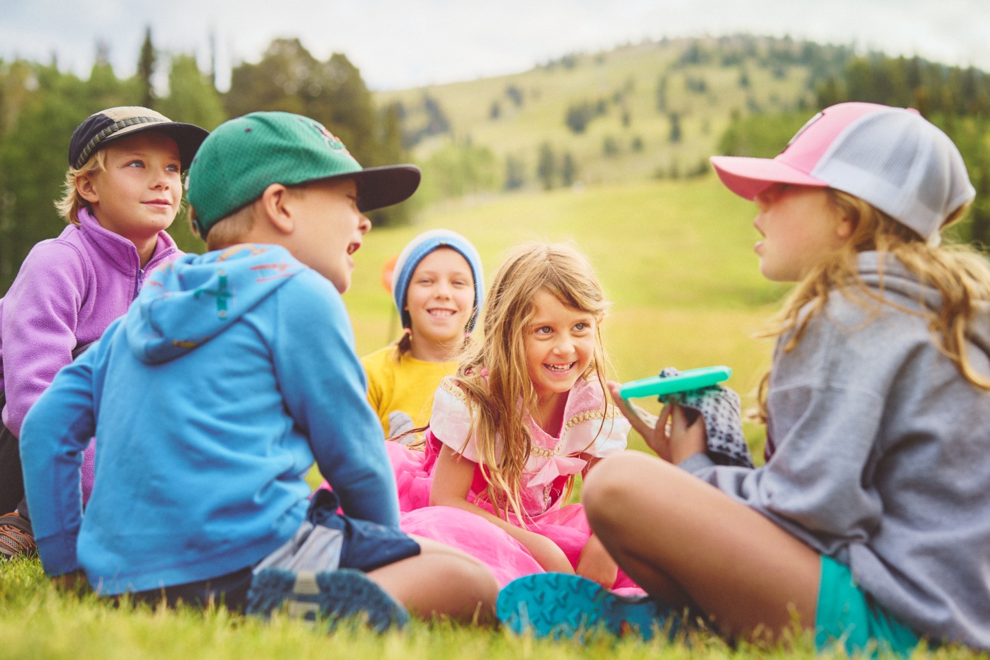 A group of kids sitting and playing at the base of a mountain