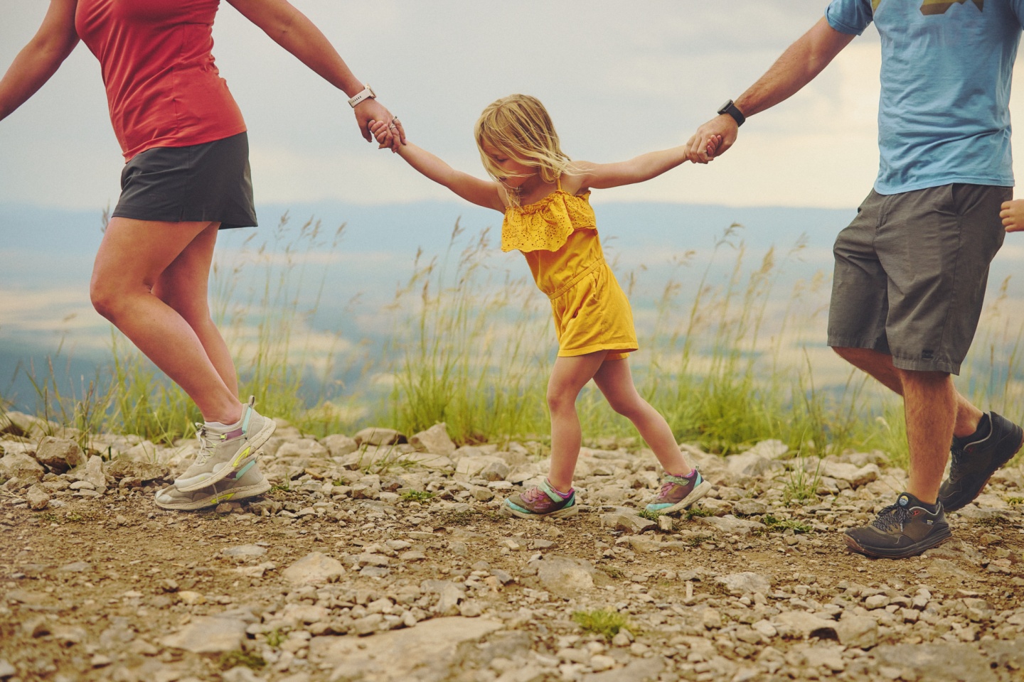 A family of three holding hands walking along a trail
