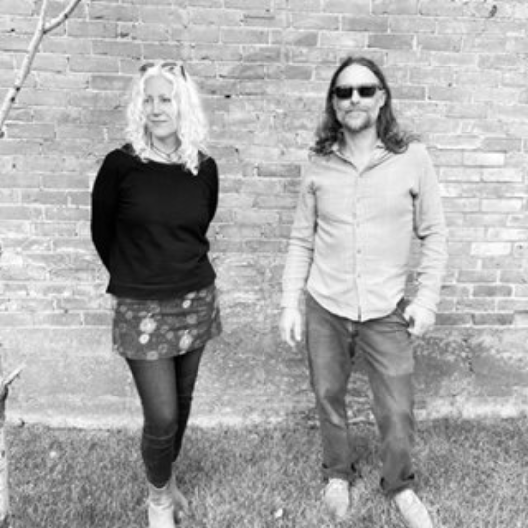 Two people standing in front of a brick wall, smiling.