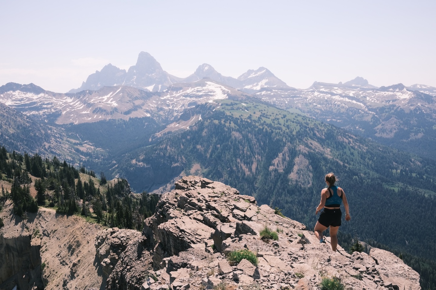 Hiker on rocky cliff overlooking snowy mountain range.