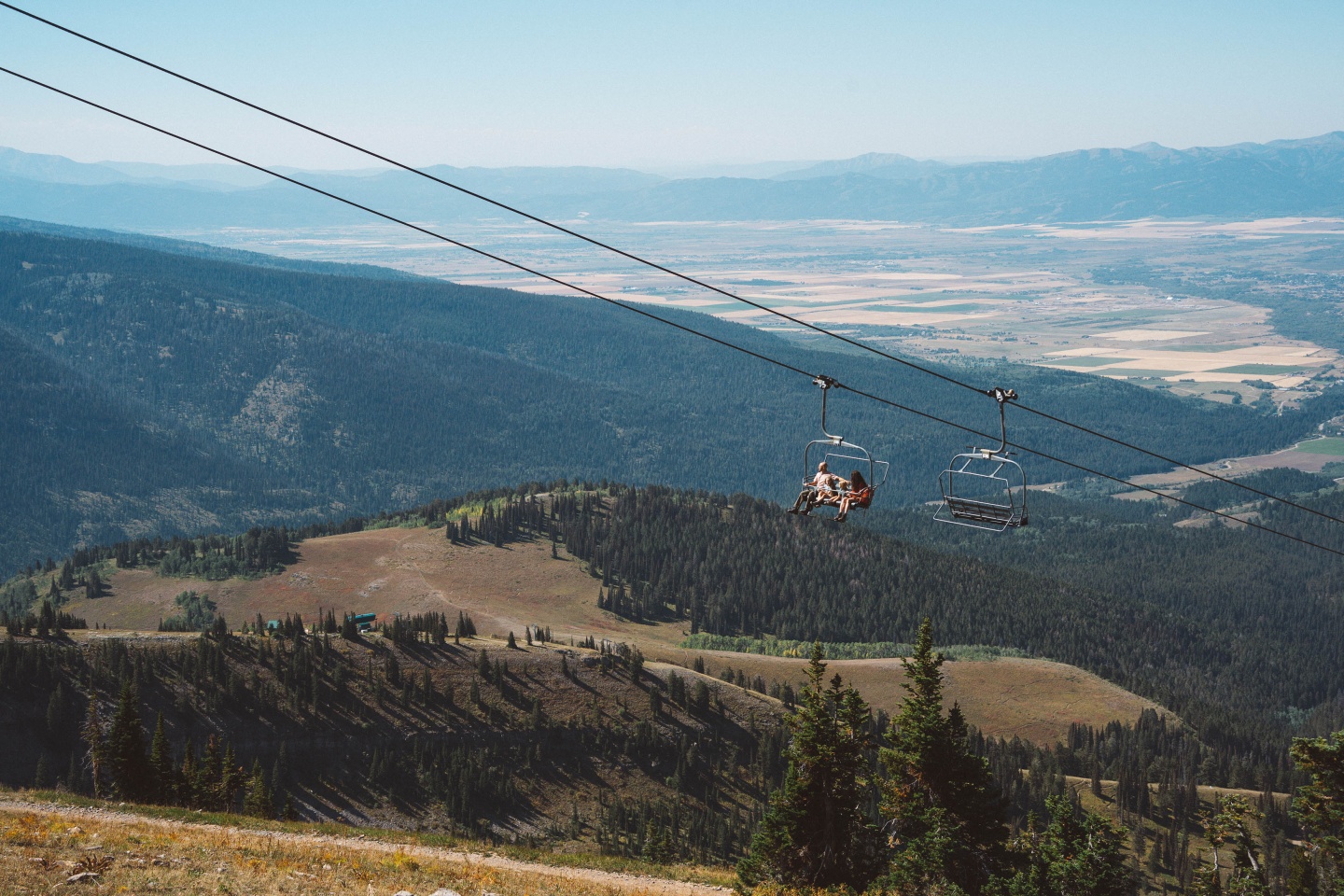 Chairlift over a scenic mountain landscape with distant valleys and blue sky.