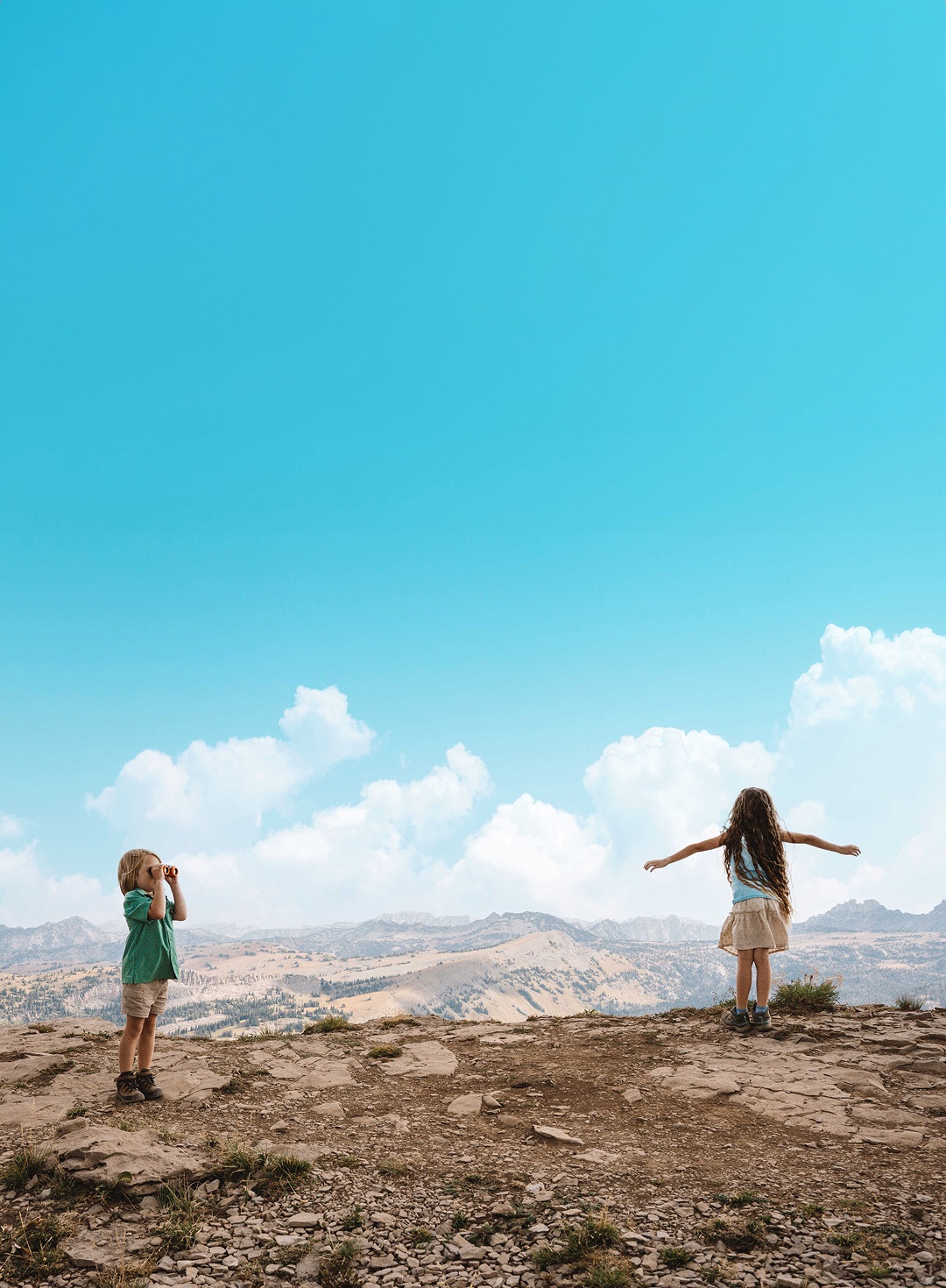 Two children on a rocky hilltop under a bright blue sky.