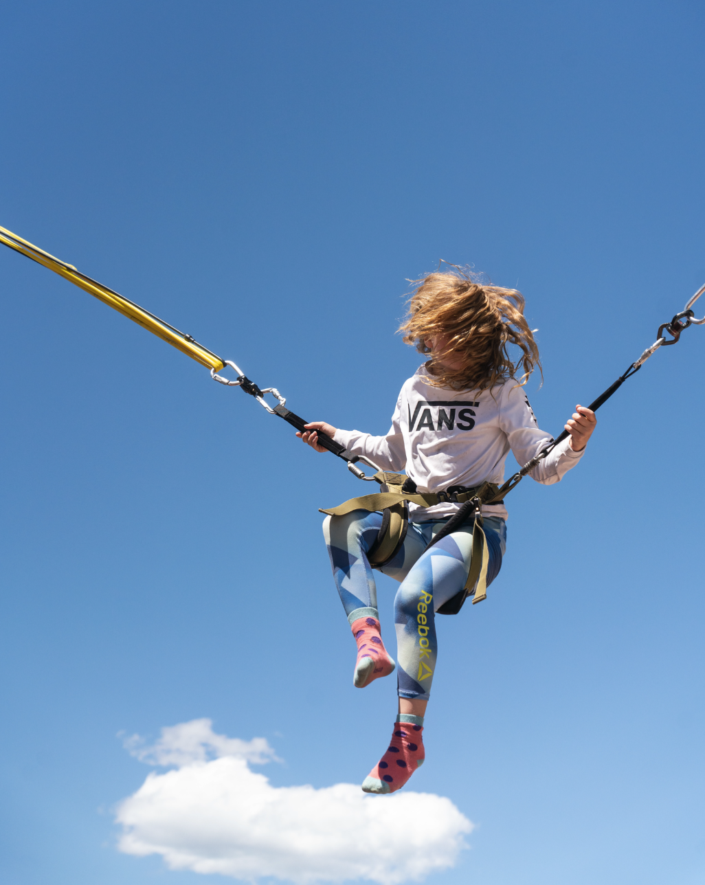 Child bungee jumping against a clear blue sky.