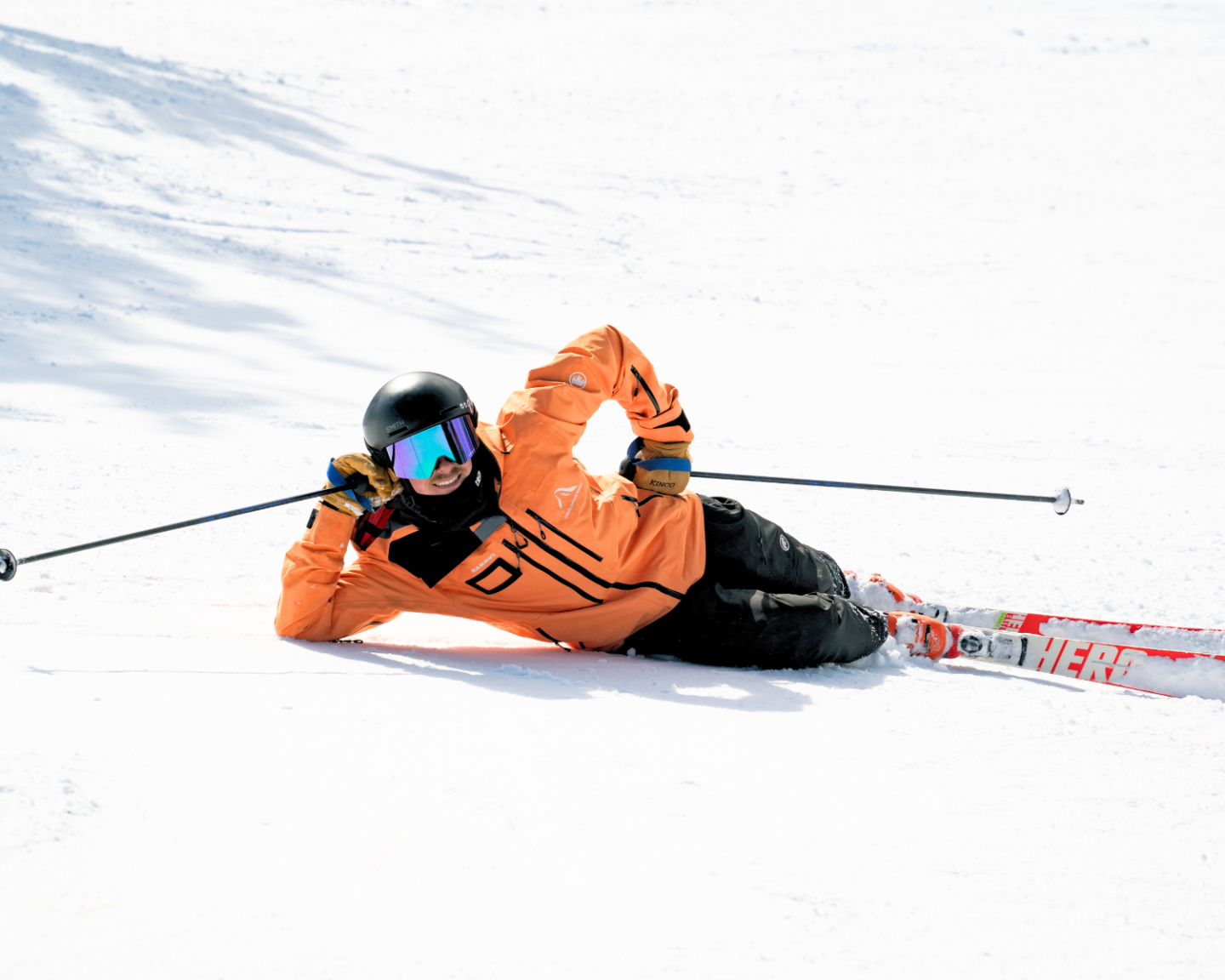 Skier in orange jacket poses playfully on snowy slope.