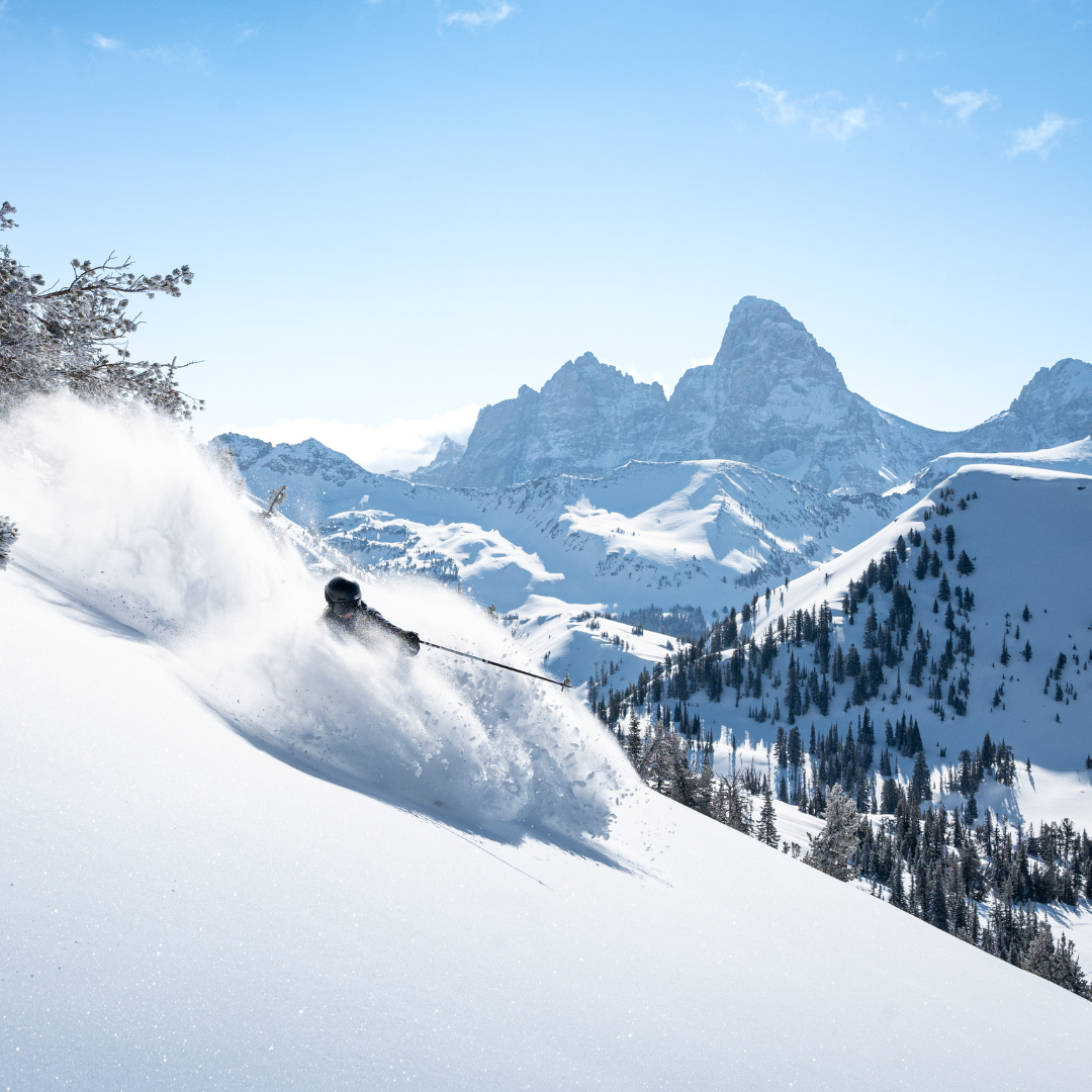 Skier gliding down snowy mountain with distant peaks.