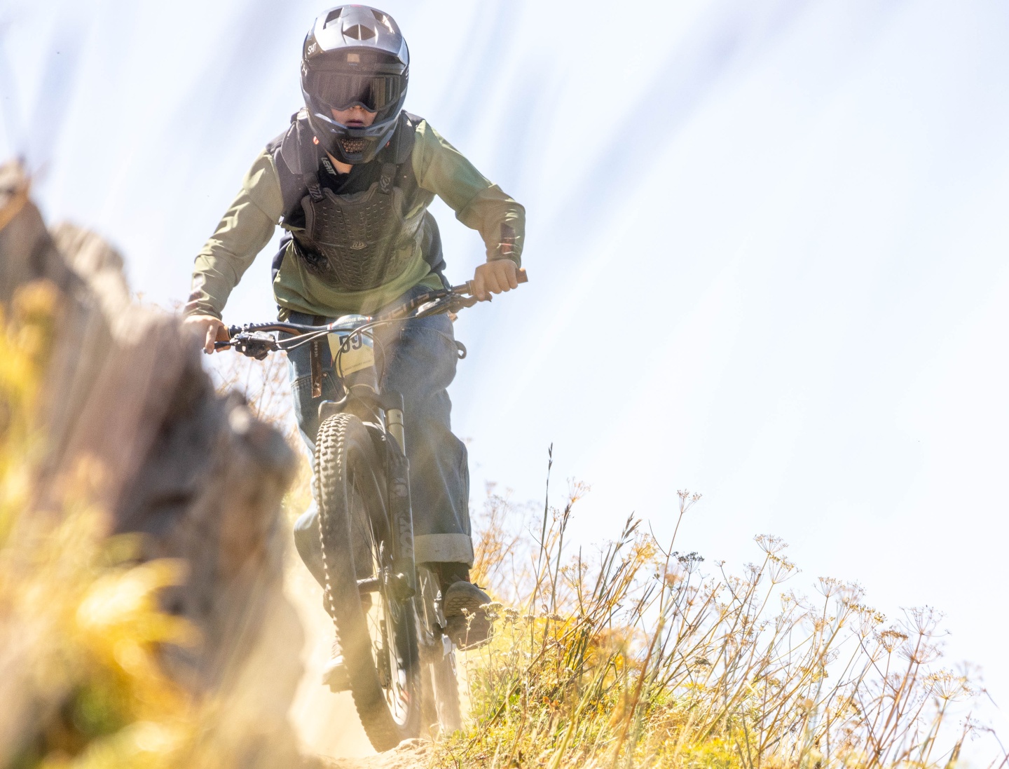 Mountain biker racing down a sunny trail, surrounded by tall grasses.