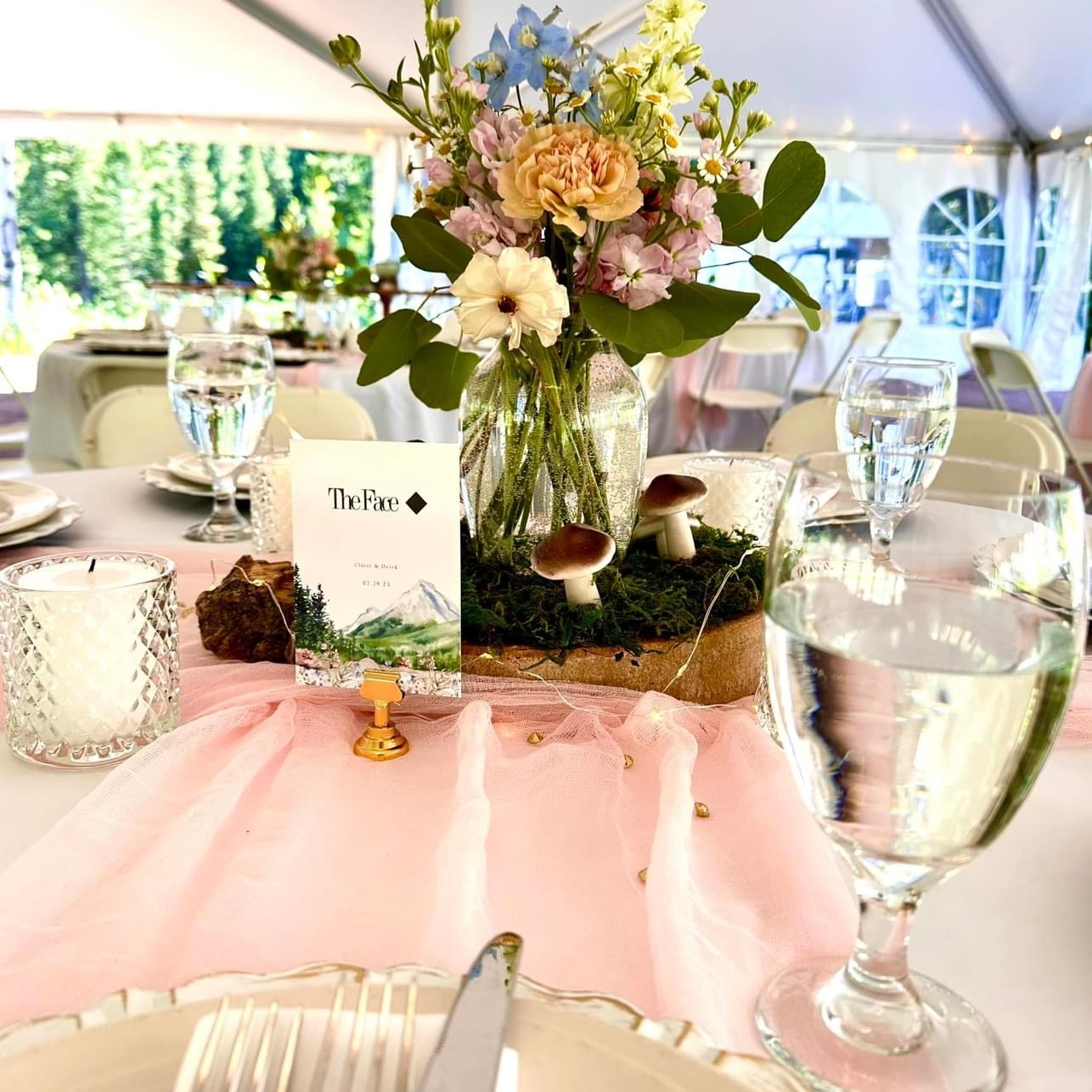 Wedding table setting with flowers and glassware under a tent.