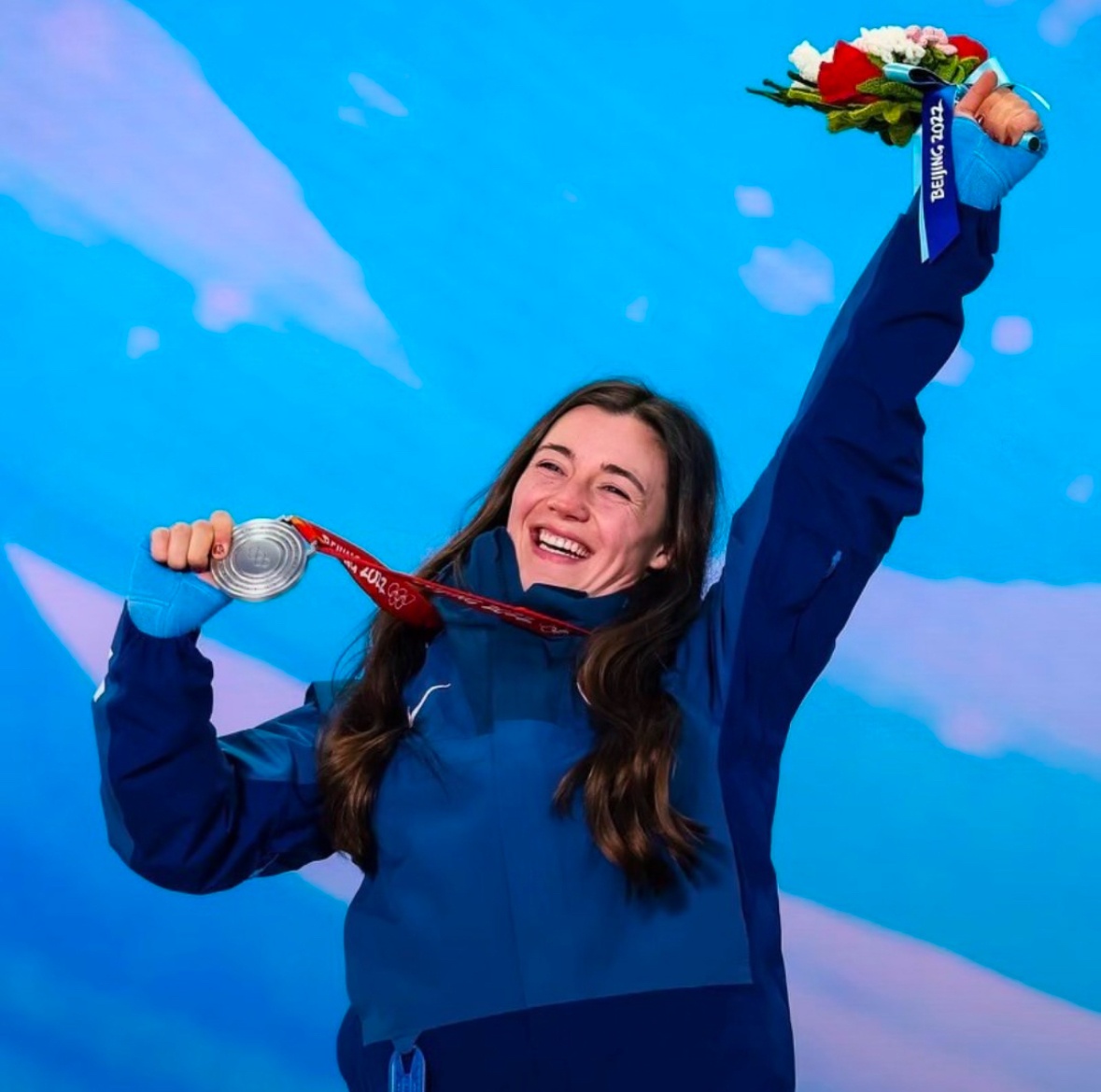 Athlete in blue celebrates, holding a medal and flowers, against a blue backdrop.