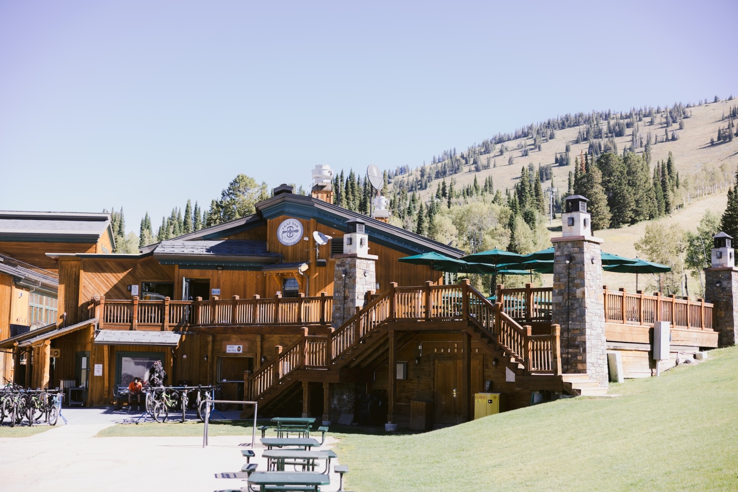 Lodge with wooden decks, outdoor seating, and forested hills in the background.