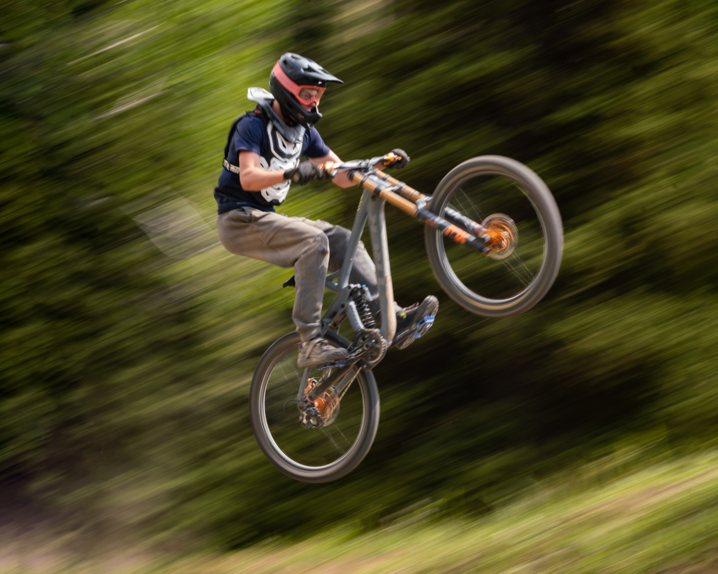 Mountain biker mid-jump on forest trail, wearing a helmet and protective gear.