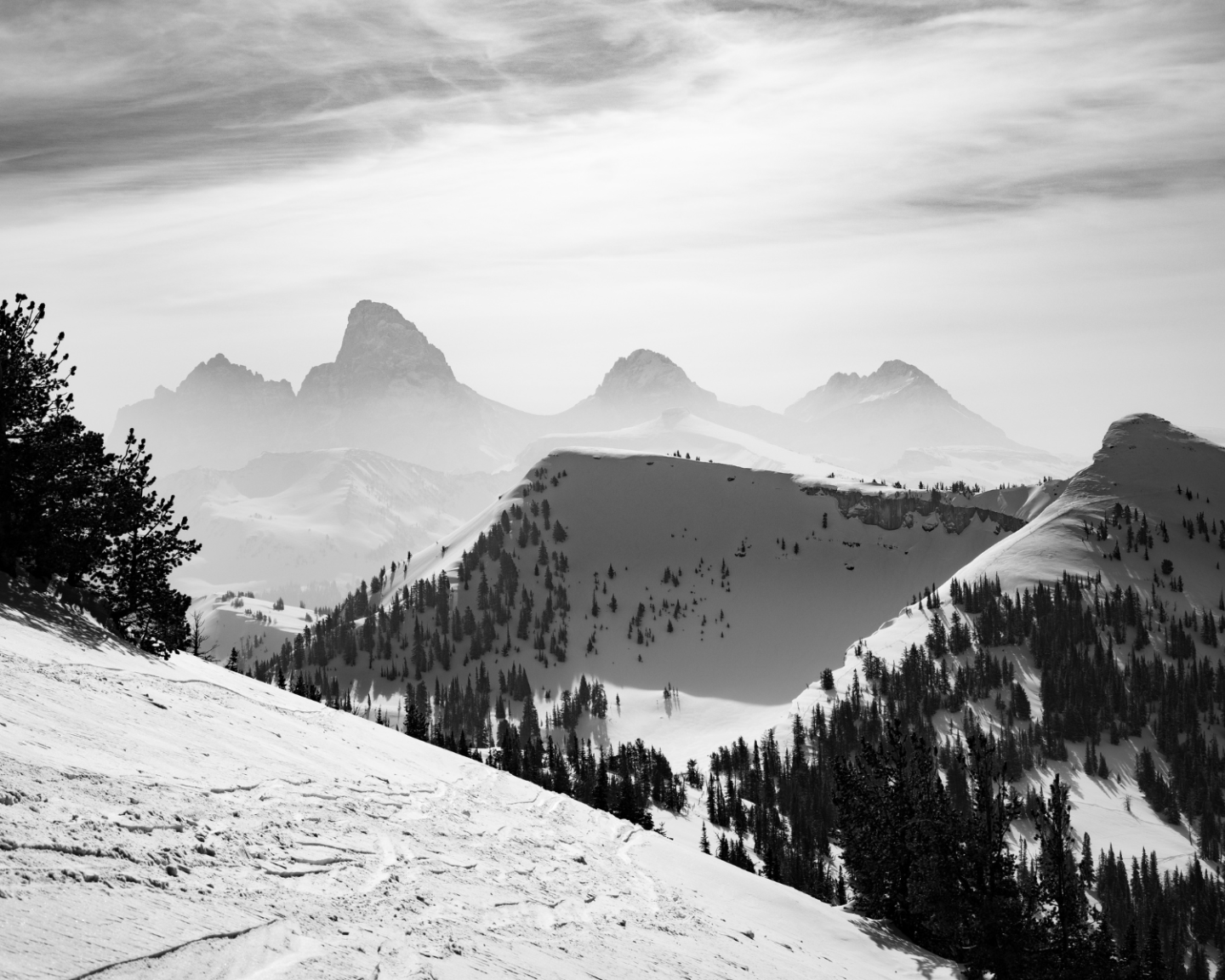 Snowy mountain landscape with distant peaks under a cloudy sky, in black and white.