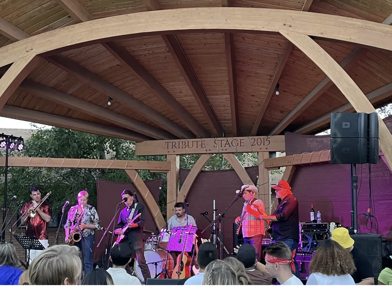 Band performing under a wooden pavilion at an outdoor stage.