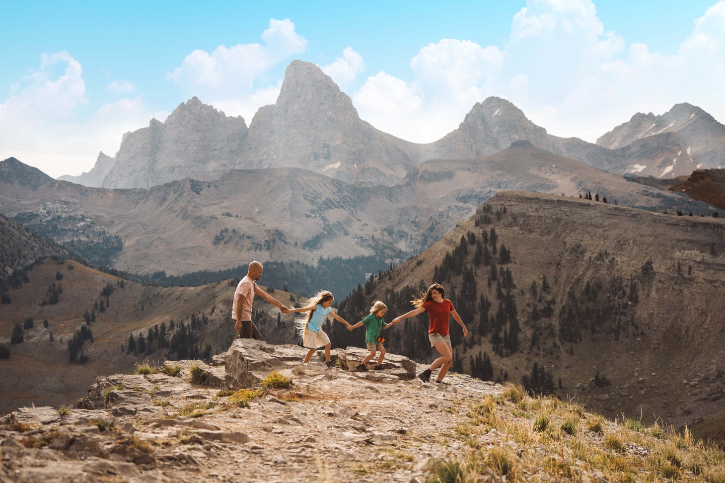 Four people hiking on a rocky mountain with jagged peaks in the background.