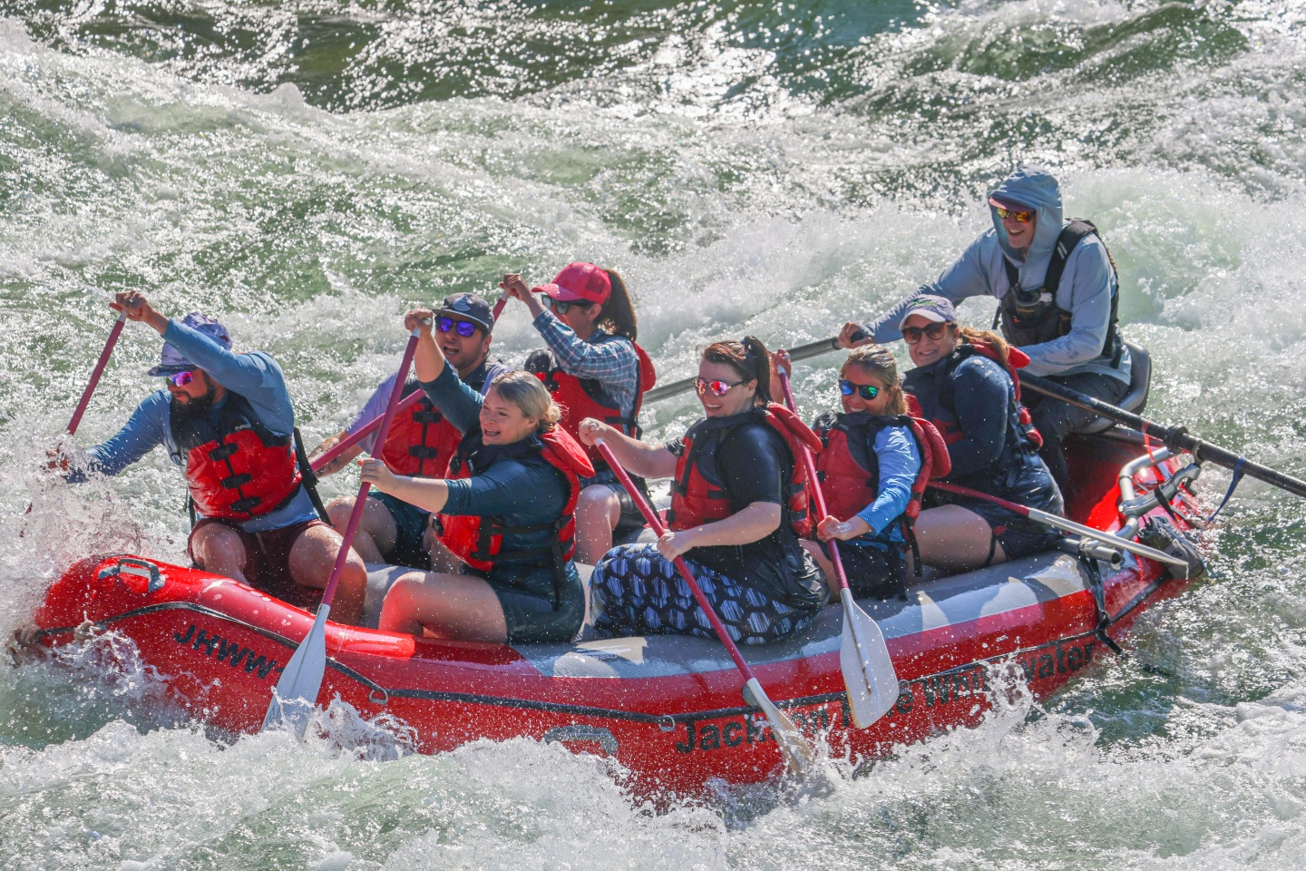 Rafting group paddles through whitewater rapids in a red inflatable raft.