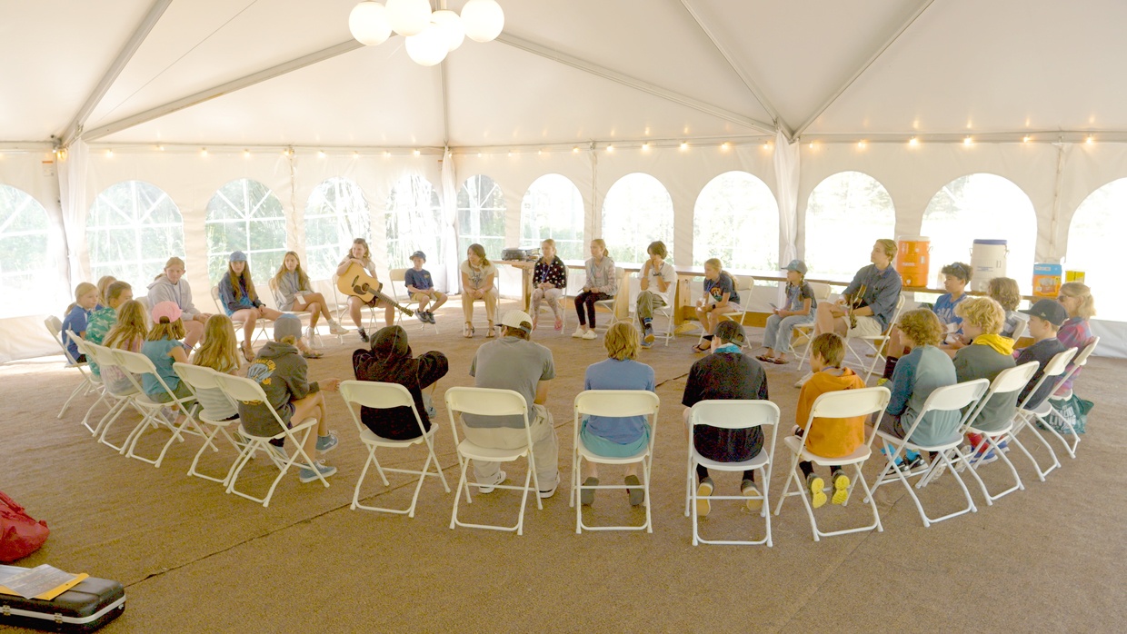 Group sitting in a circle in a white tent with string lights.