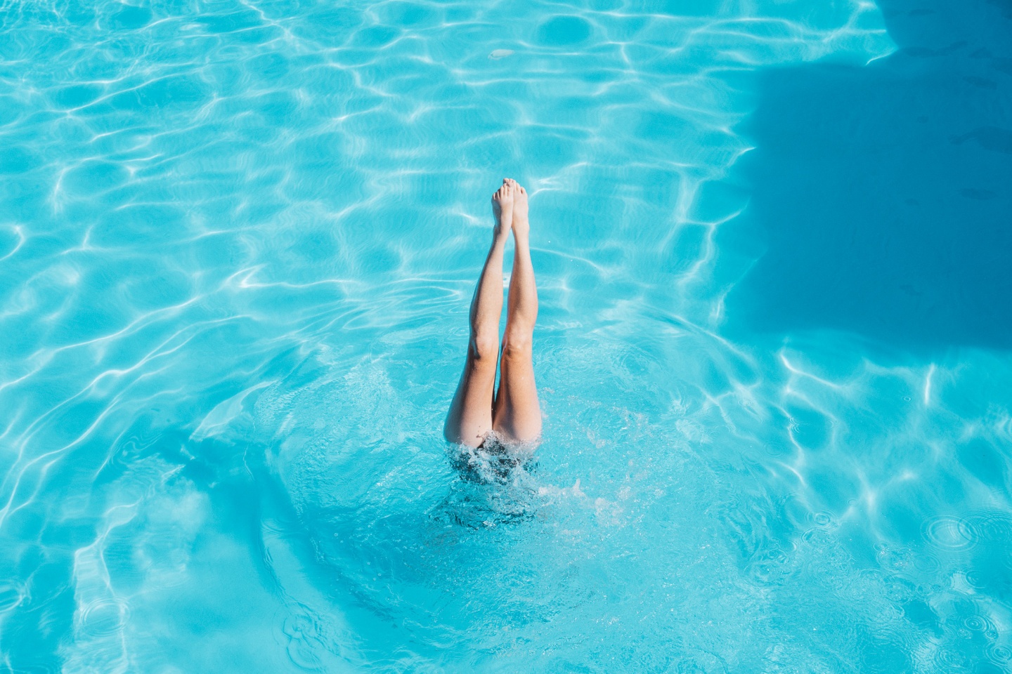 Diver's legs above water in a sunny pool.