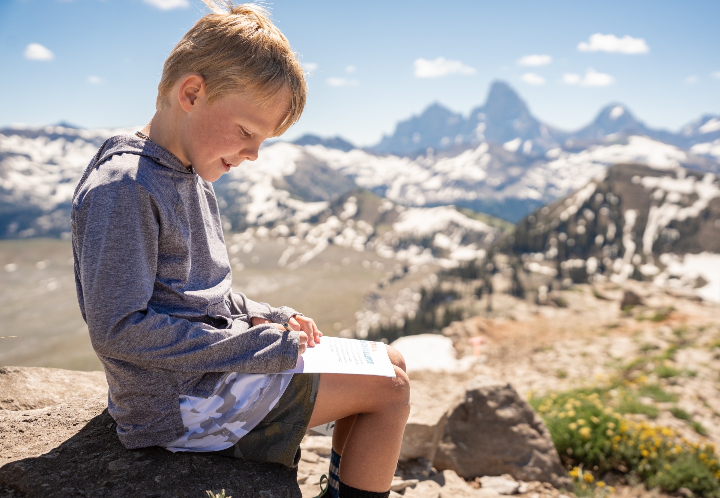 Boy reading outdoors with mountains in the background.