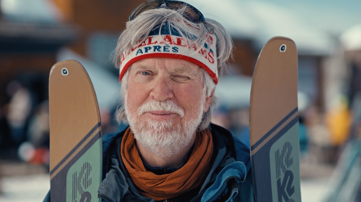 Elderly man with skis, wearing a headband, in a snowy setting.