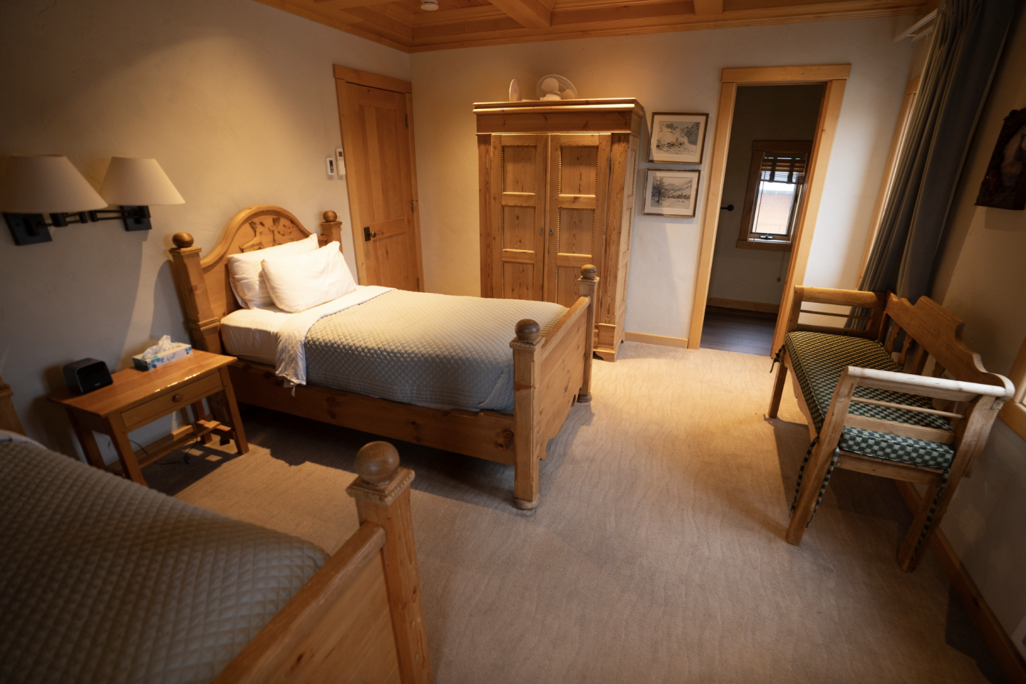 Cozy bedroom with two wooden beds, nightstand, and wardrobe. Warm lighting fills the room.