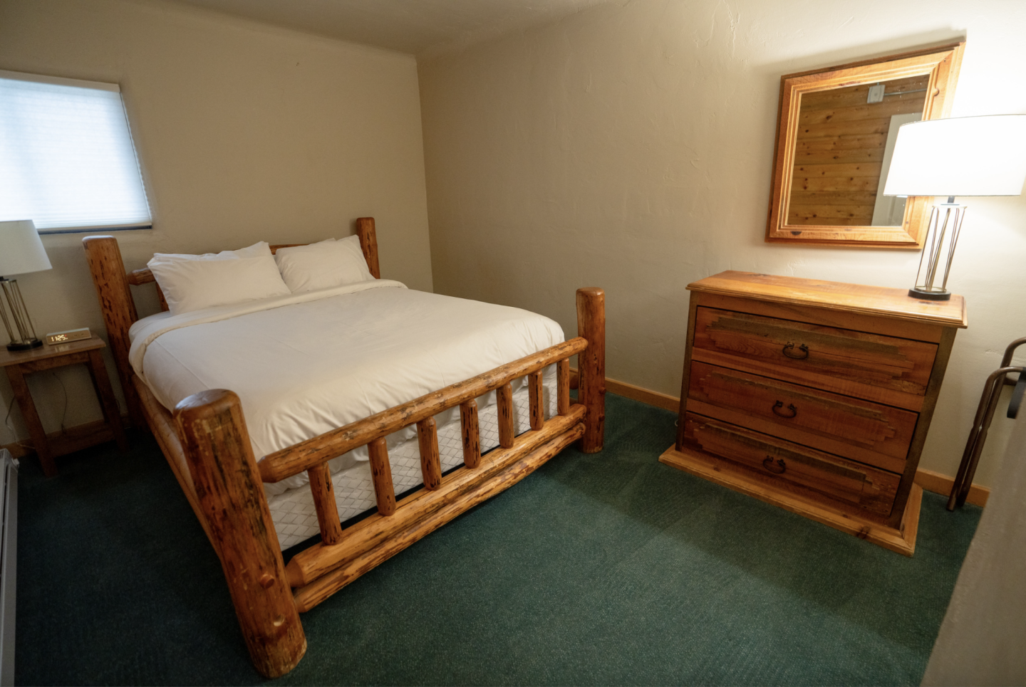Cozy bedroom with wooden bed and dresser, carpeted floor, and table lamp.