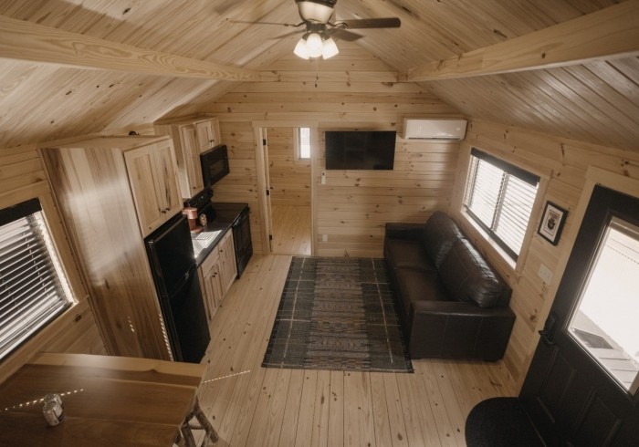 Cozy wooden cabin interior with kitchen, sofa, and TV. Ceiling fan above.