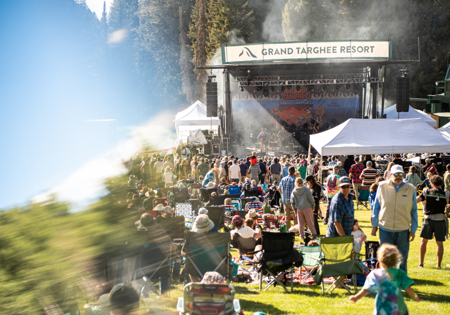 Outdoor concert with crowd near mountains, sunny day.