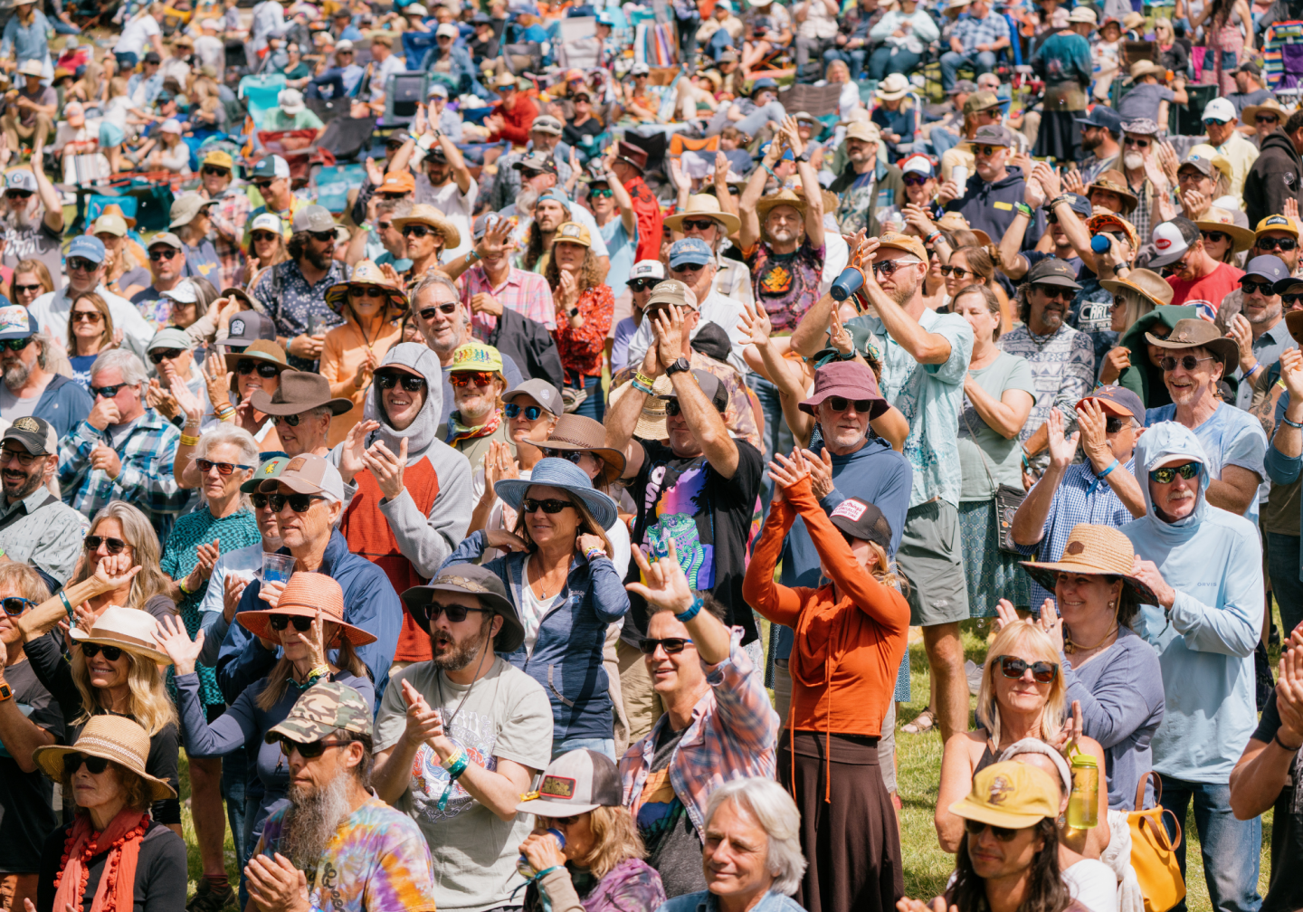 Crowd at outdoor event clapping, wearing hats and sunglasses.