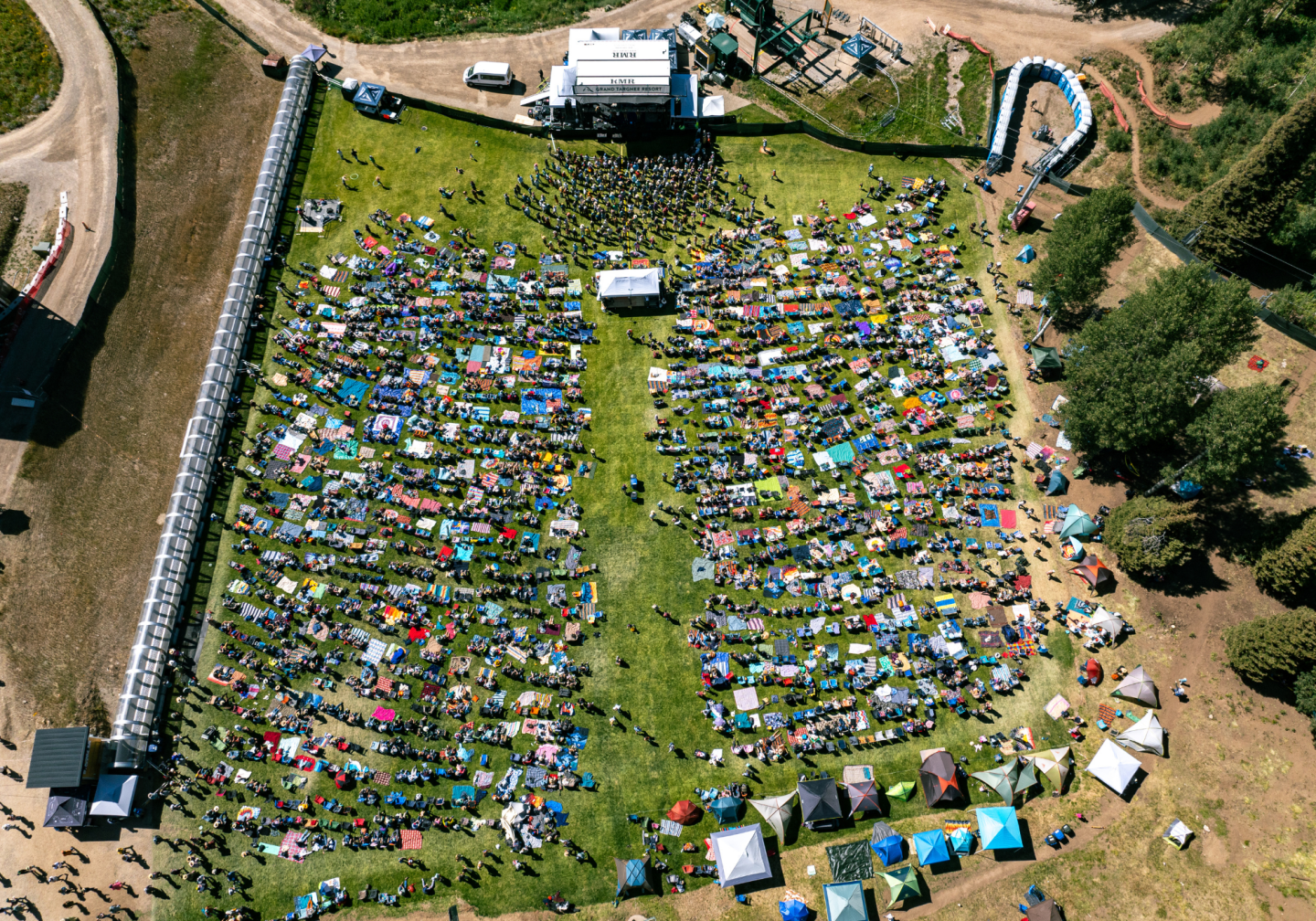 Aerial view of a crowded outdoor concert with a stage and scattered tents.