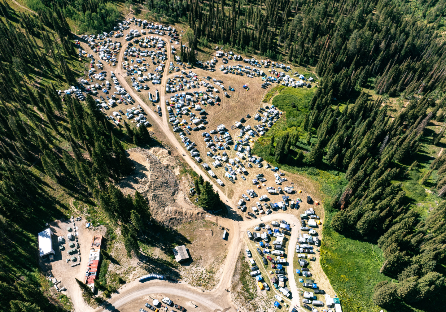 Aerial view of a forest campsite with numerous tents and vehicles.