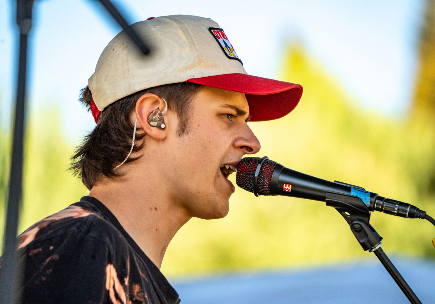 Singer wearing a cap performing outdoors with a microphone.