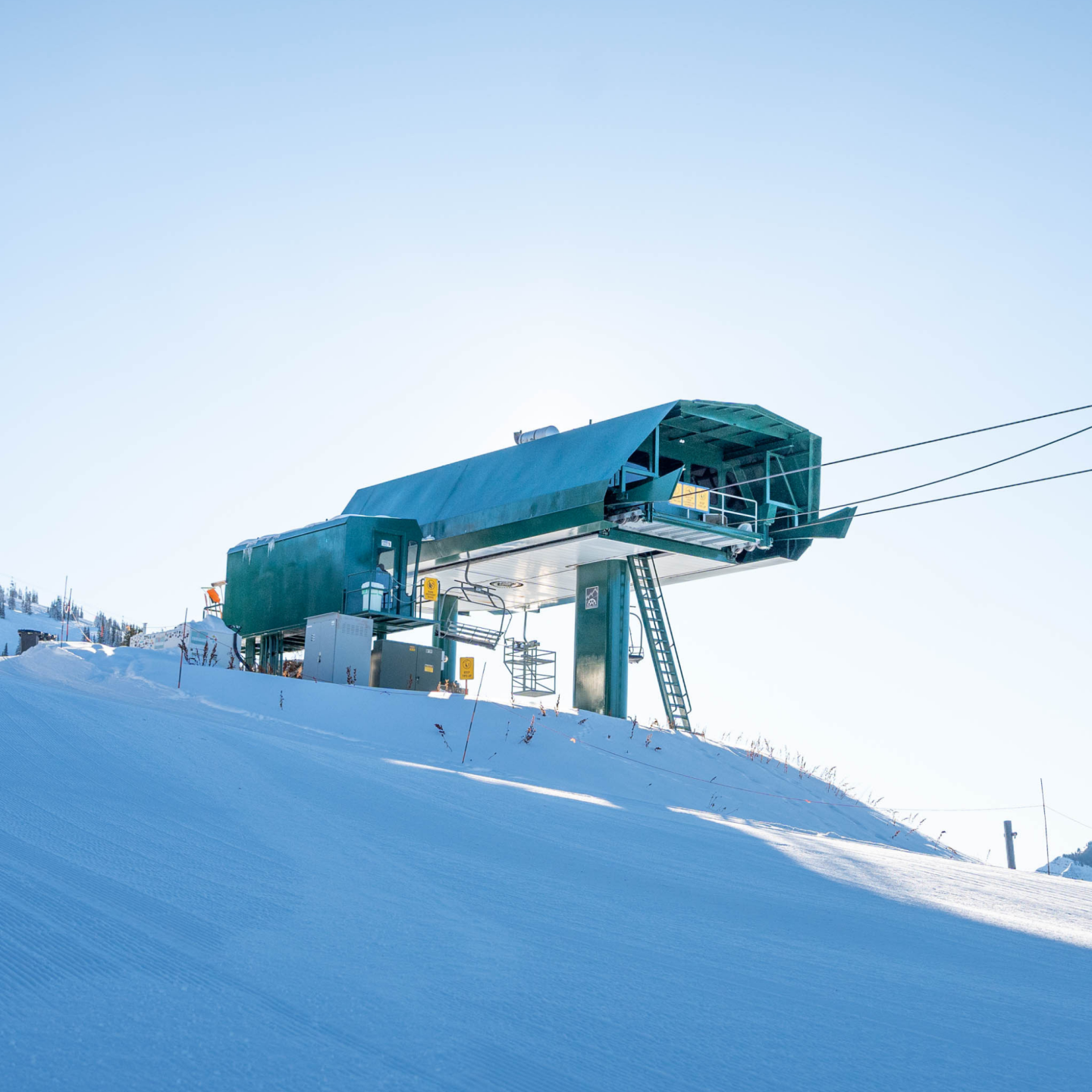 Ski lift station on a snowy slope under a clear blue sky.