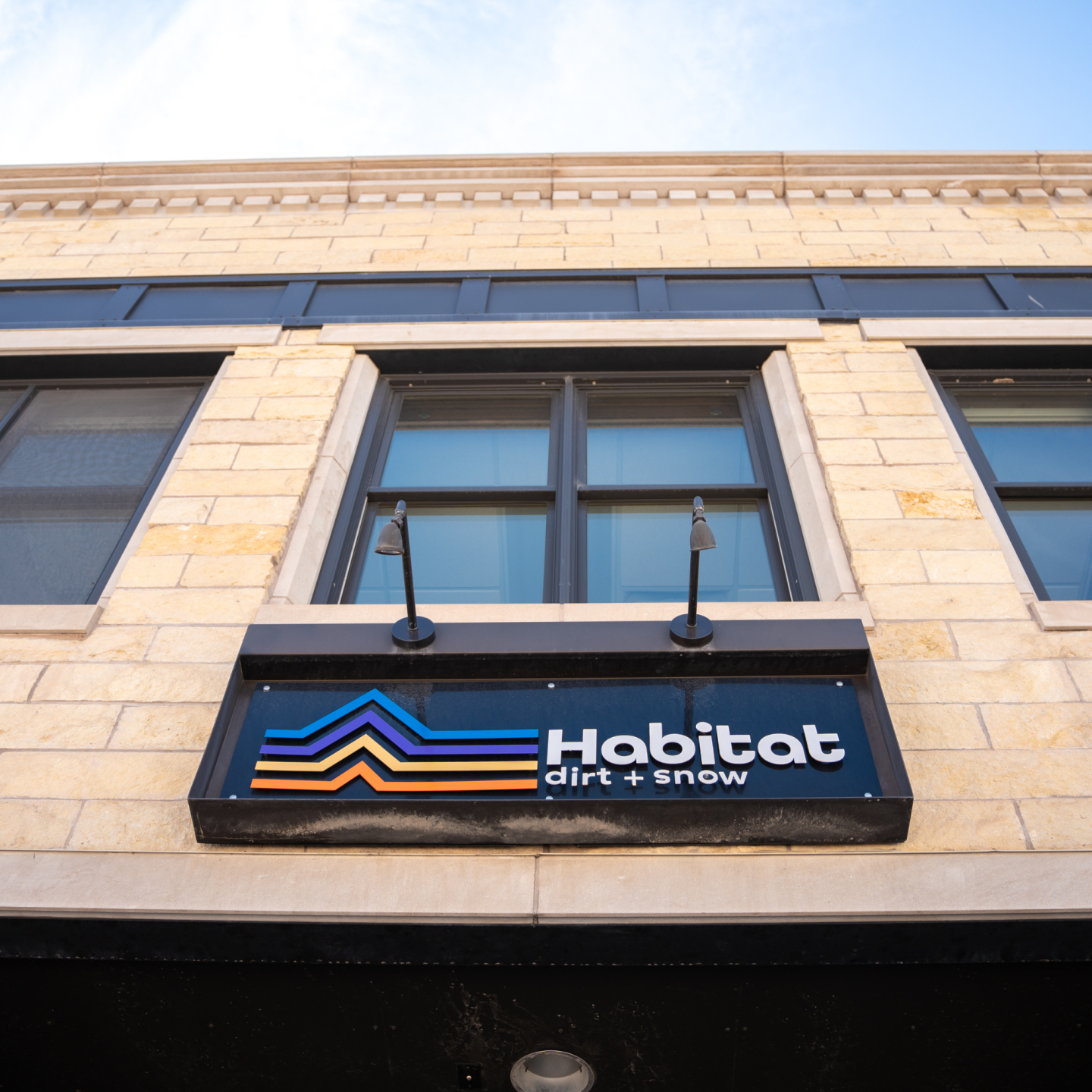 Outdoor sign on beige brick building under two windows.