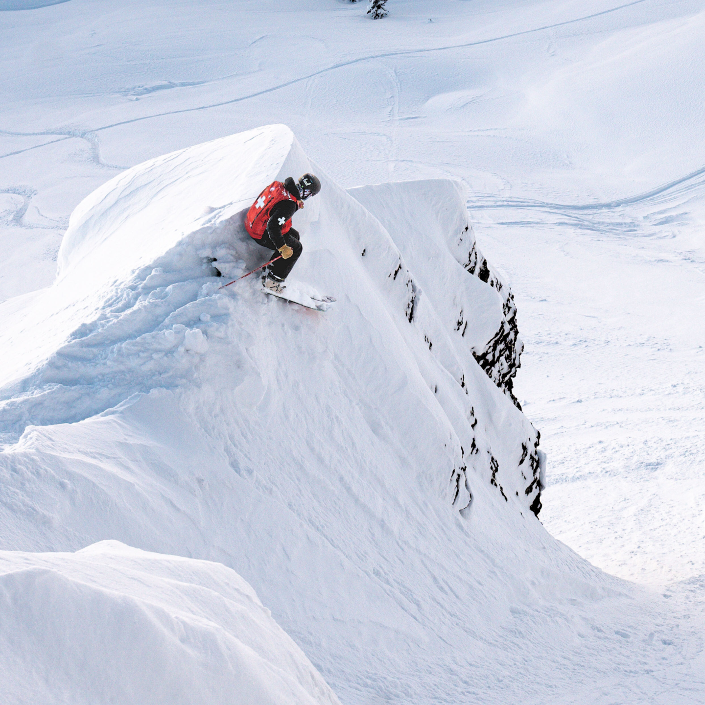 Snowboarder descending a snowy cliff in bright sunlight.