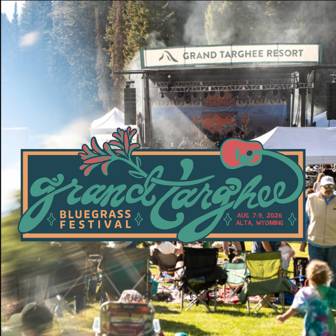 Festival crowd relaxing outdoors near a stage under trees.