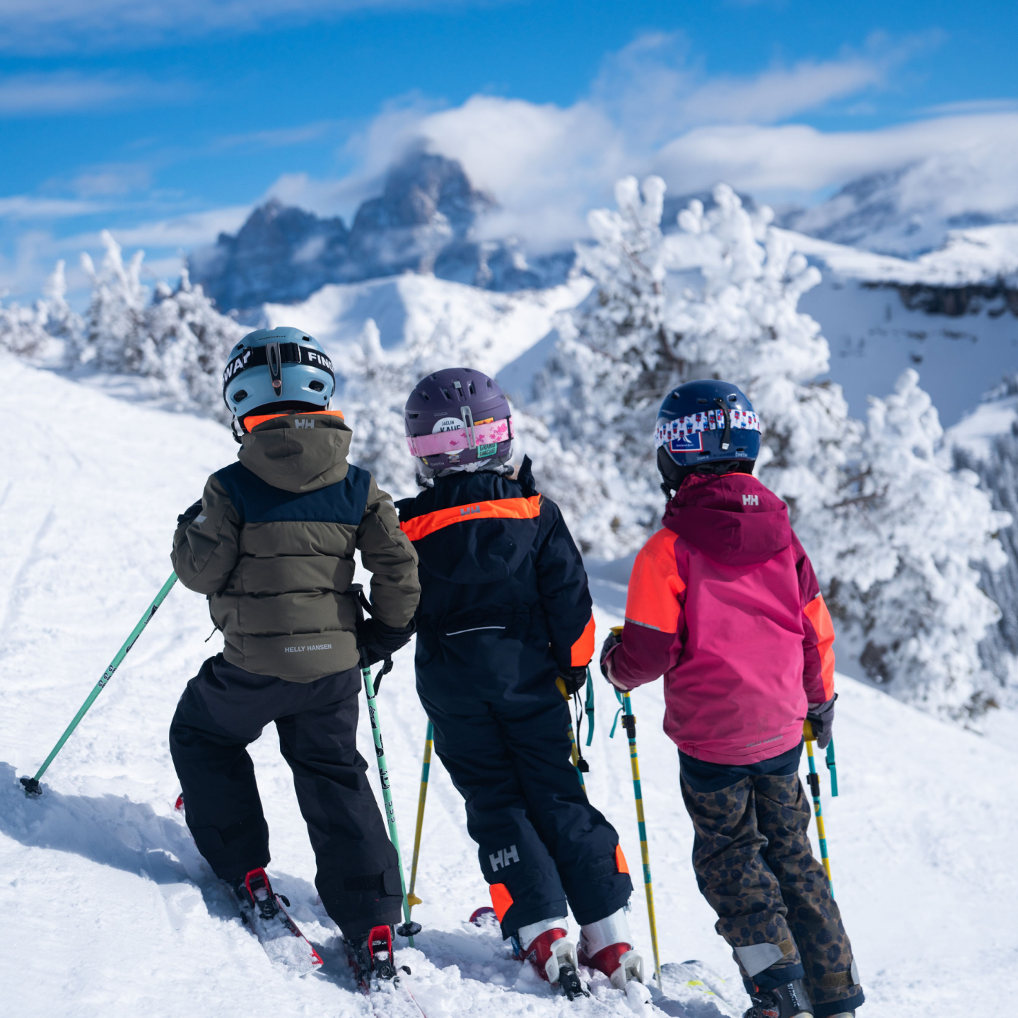 Three children skiing on a snowy mountain slope under a clear blue sky.