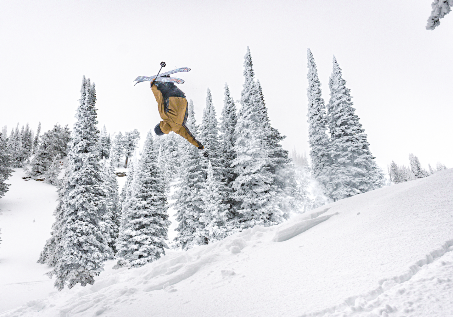 Snowboarder mid-jump against snowy, tree-filled backdrop.
