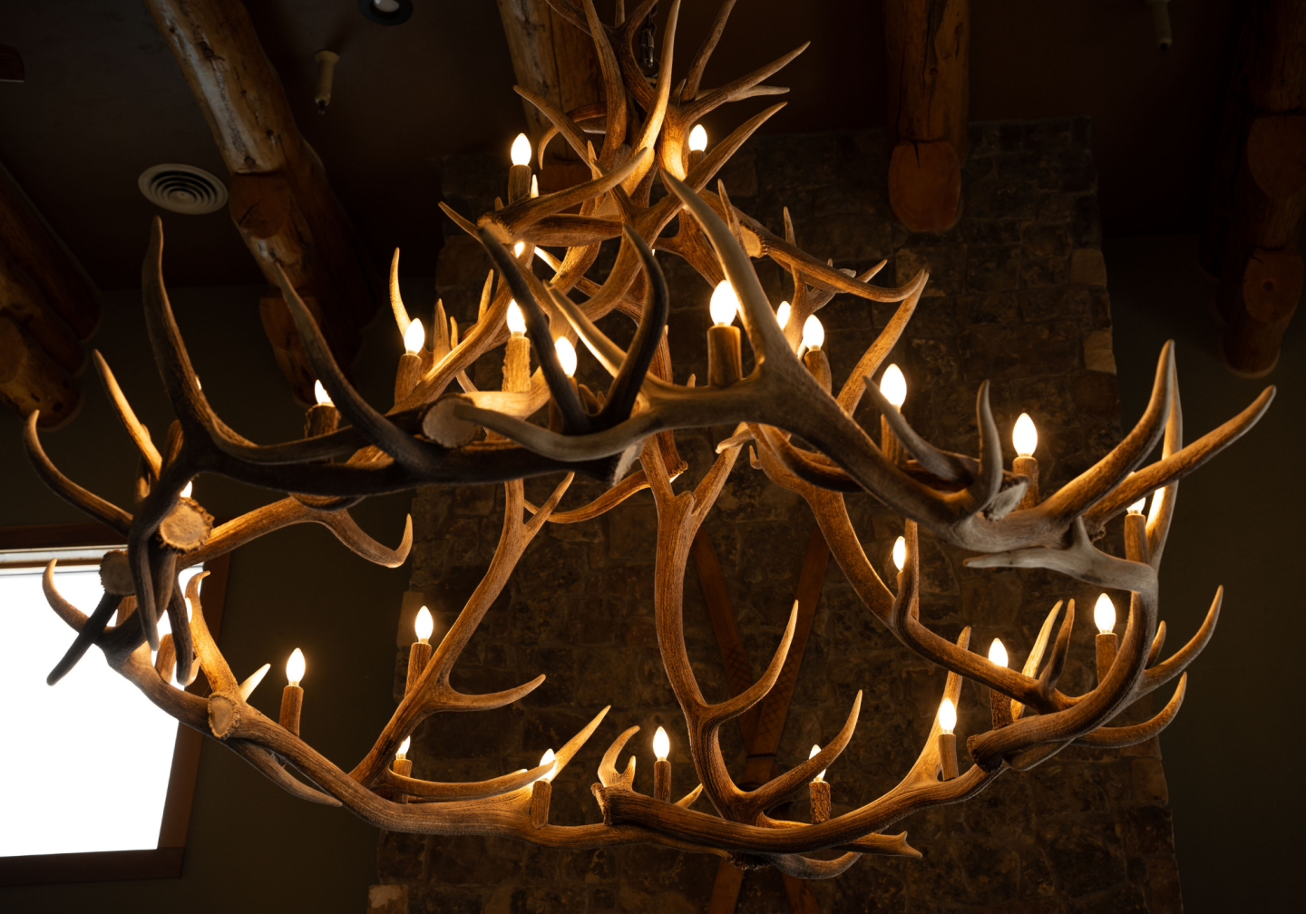 Rustic antler chandelier with glowing bulbs against a stone wall.