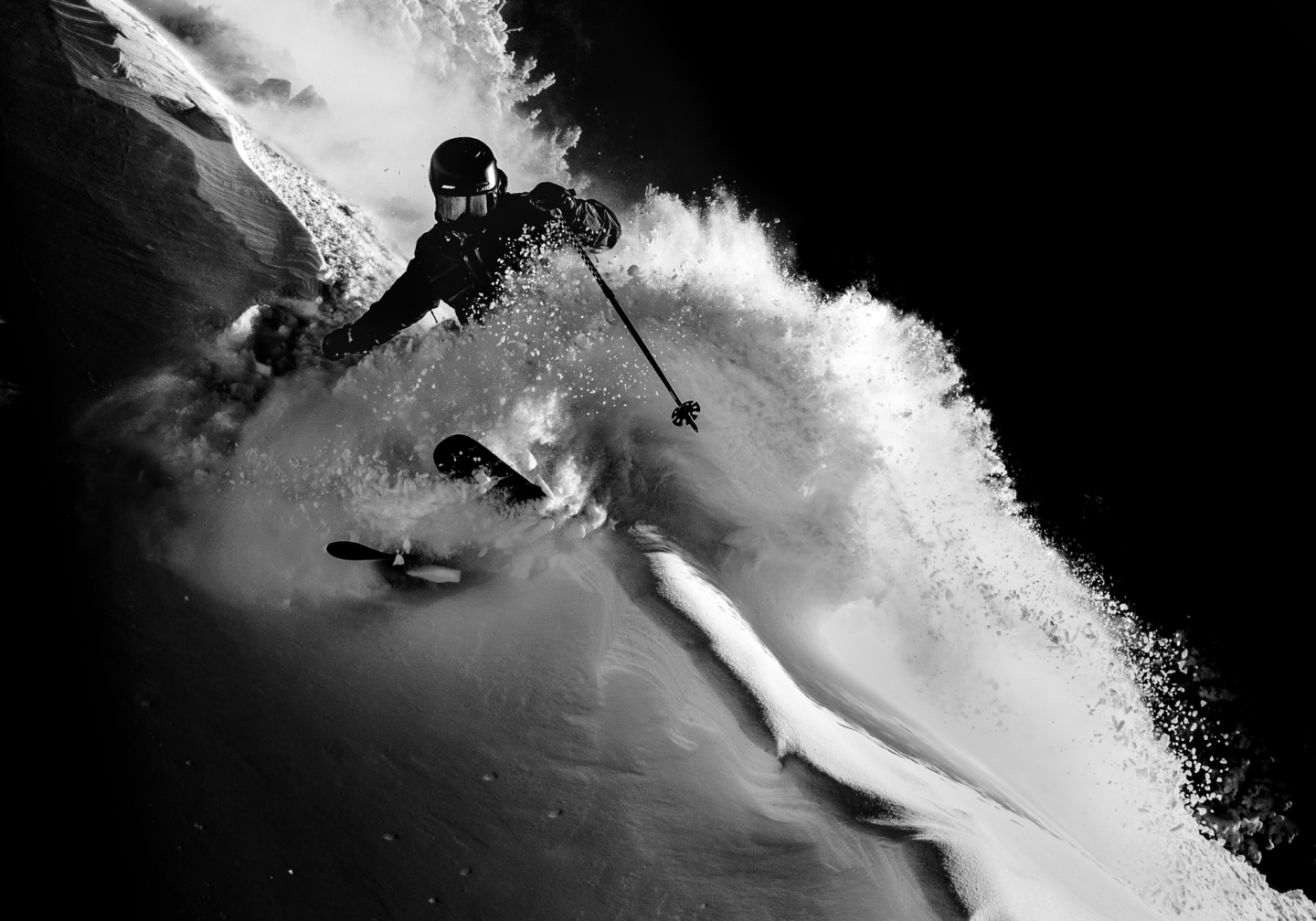 Skier carving through powder on a dark slope in black and white photograph.