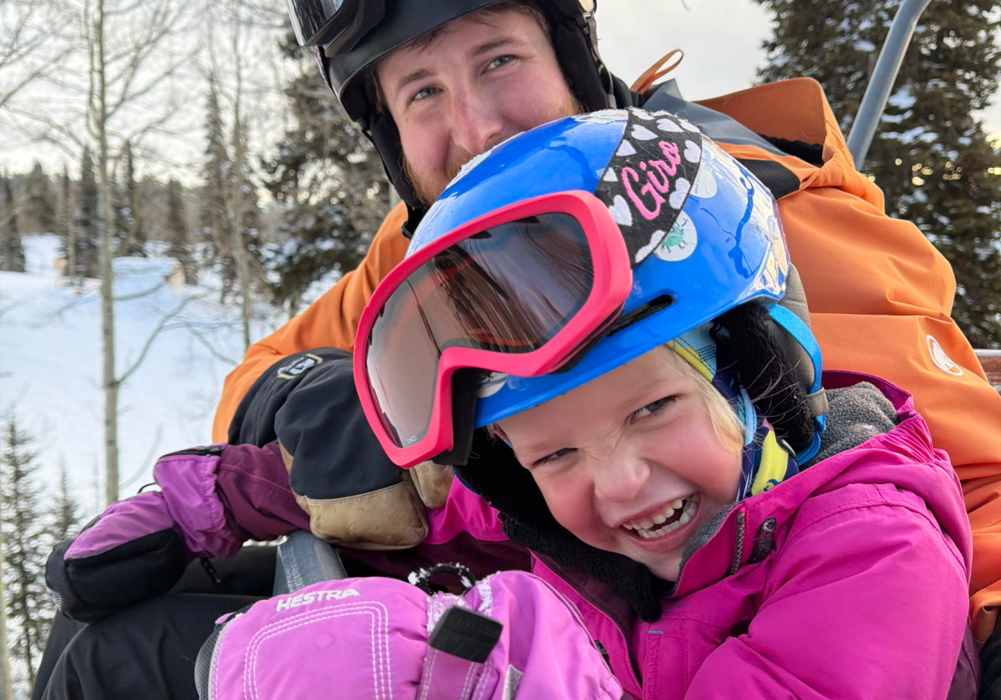 Child and adult in winter gear on a ski lift, smiling happily.