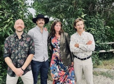 Group of four people smiling outdoors with greenery.