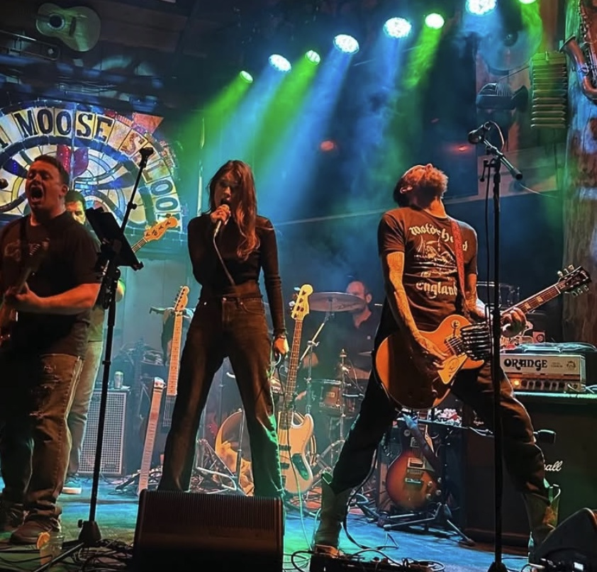 Rock band performing energetically on stage with colorful lights.